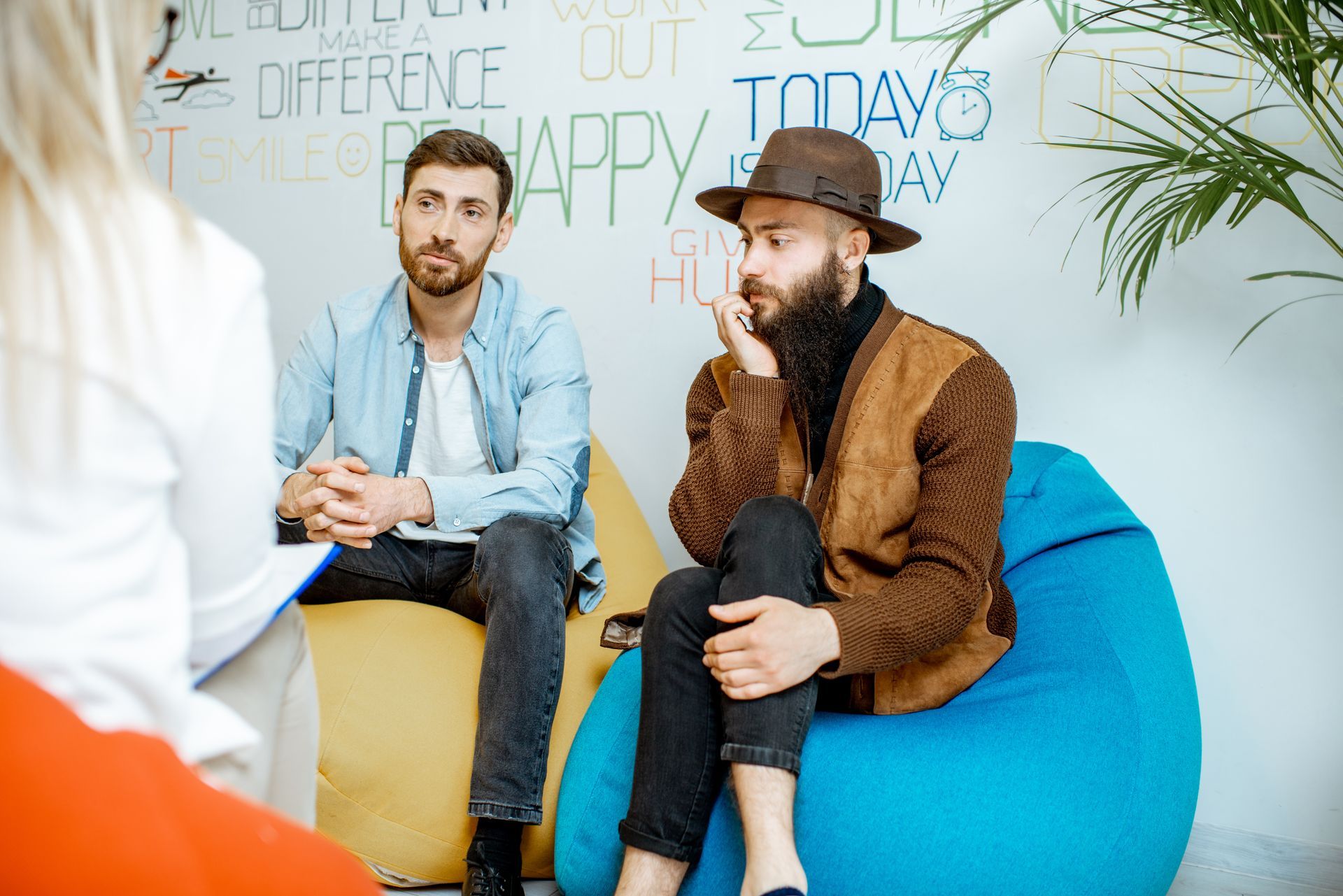 Two men in a group therapy session, one wearing a hat, the other looking on intently.