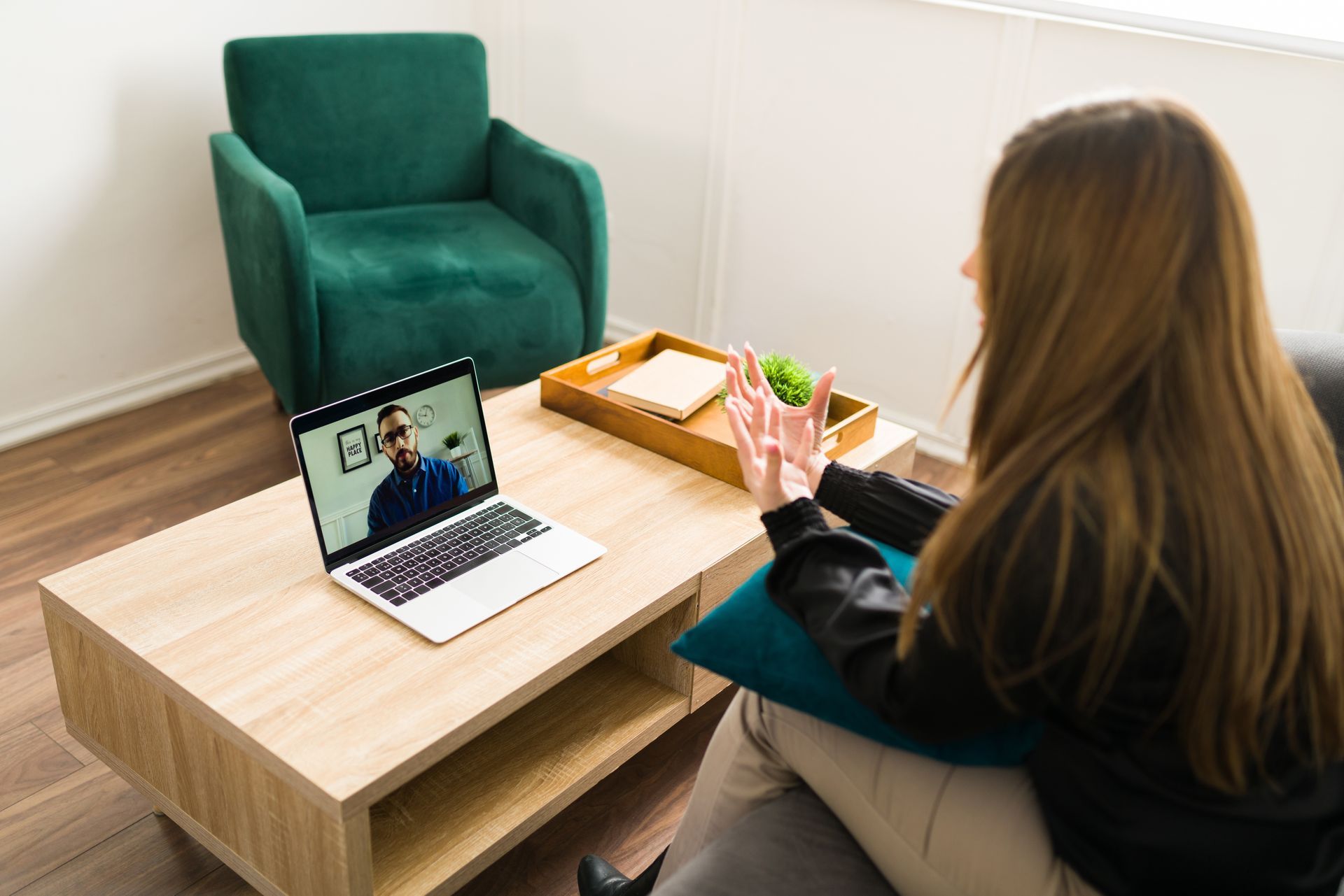 Woman in video call, gesturing while looking at laptop. Man on screen. Living room setting.
