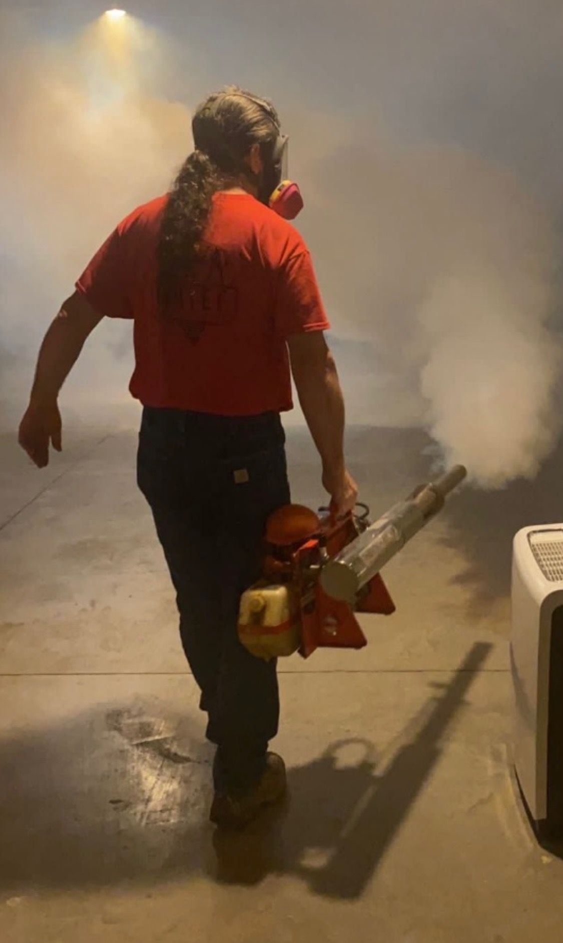 A man in a protective suit is spraying a room with a sprayer.