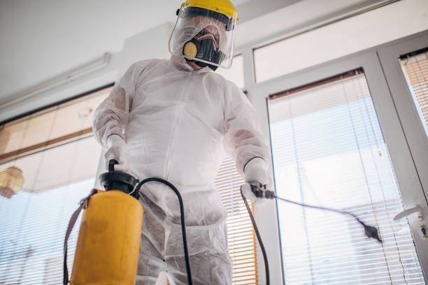 A man in a protective suit is spraying a room with a sprayer.