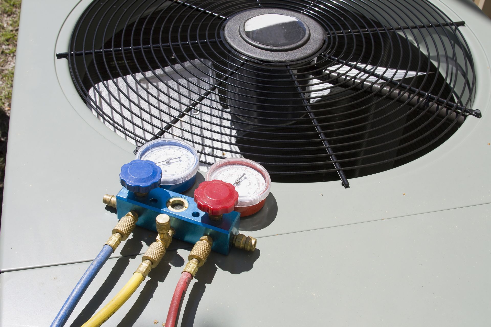 HVAC unit with a large black fan and blue, red, and white service gauges attached to yellow and black hoses