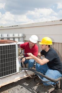 Two workers in hard hats inspecting rooftop HVAC equipment under a cloudy sky