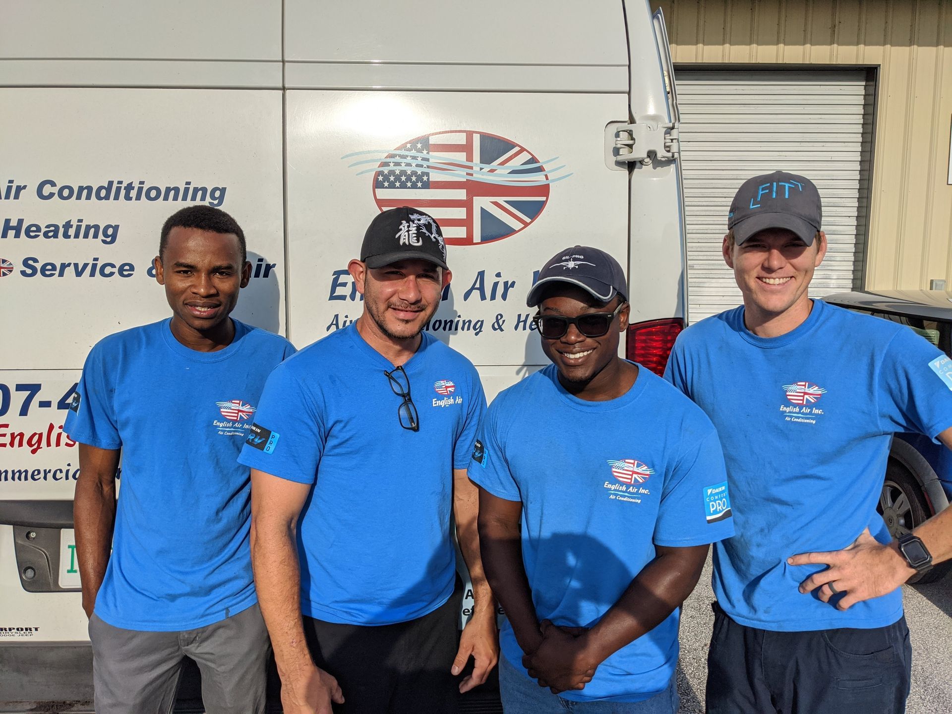 Four HVAC technicians in blue shirts posing in front of a service truck with company logo.