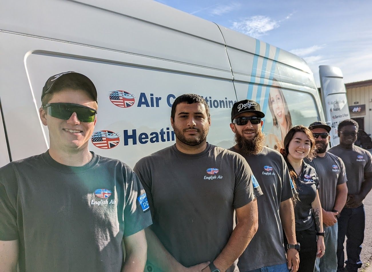 People in matching gray shirts stand in line beside a service van at an outdoor event.