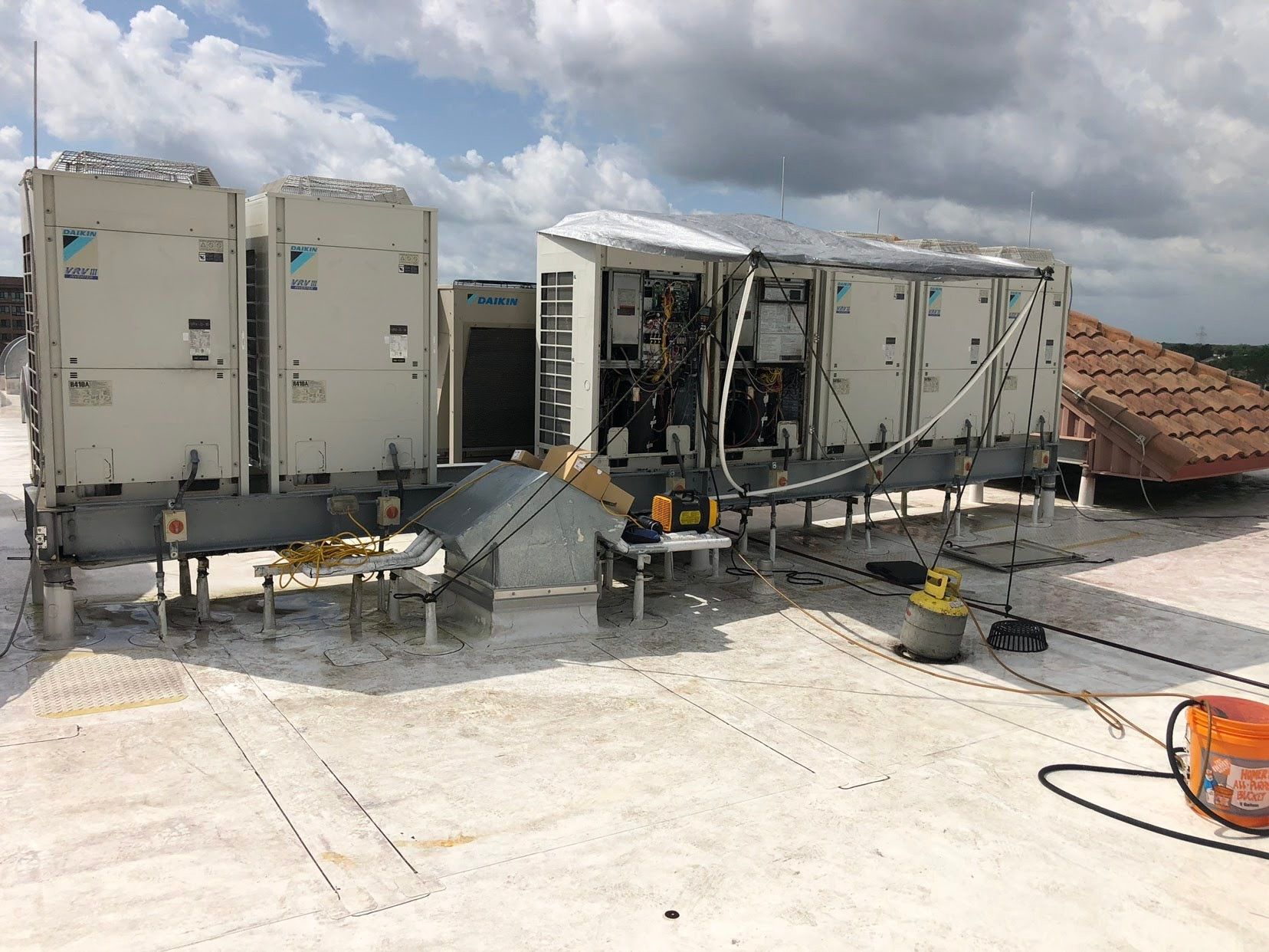 Rooftop HVAC units and ductwork on a concrete roof under a cloudy sky