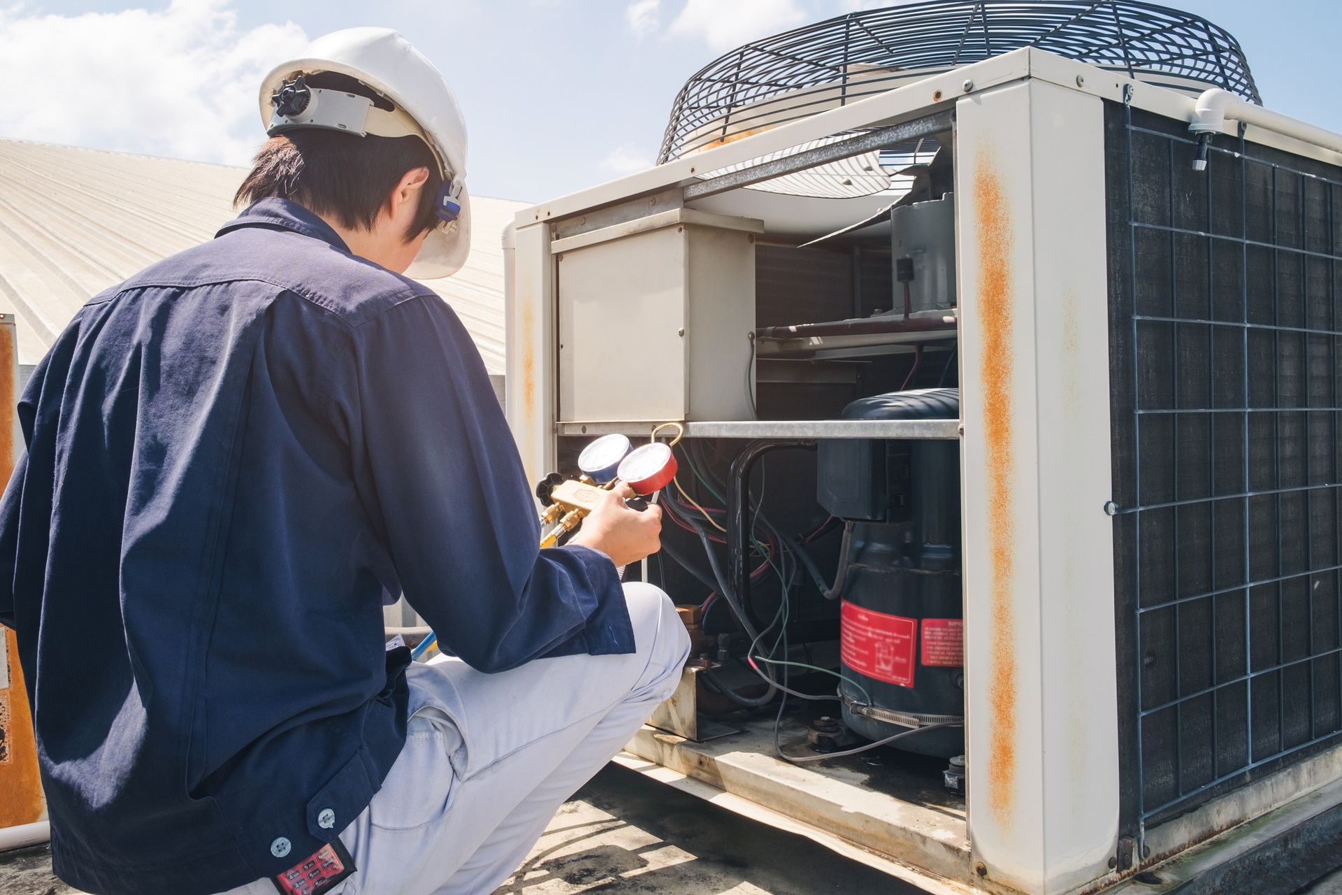 Technician inspecting an outdoor HVAC unit with tools beside a building rooftop