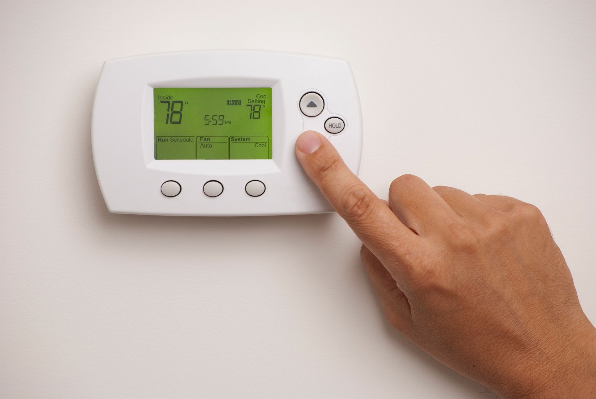 Hand adjusting a white wall thermostat with a green display