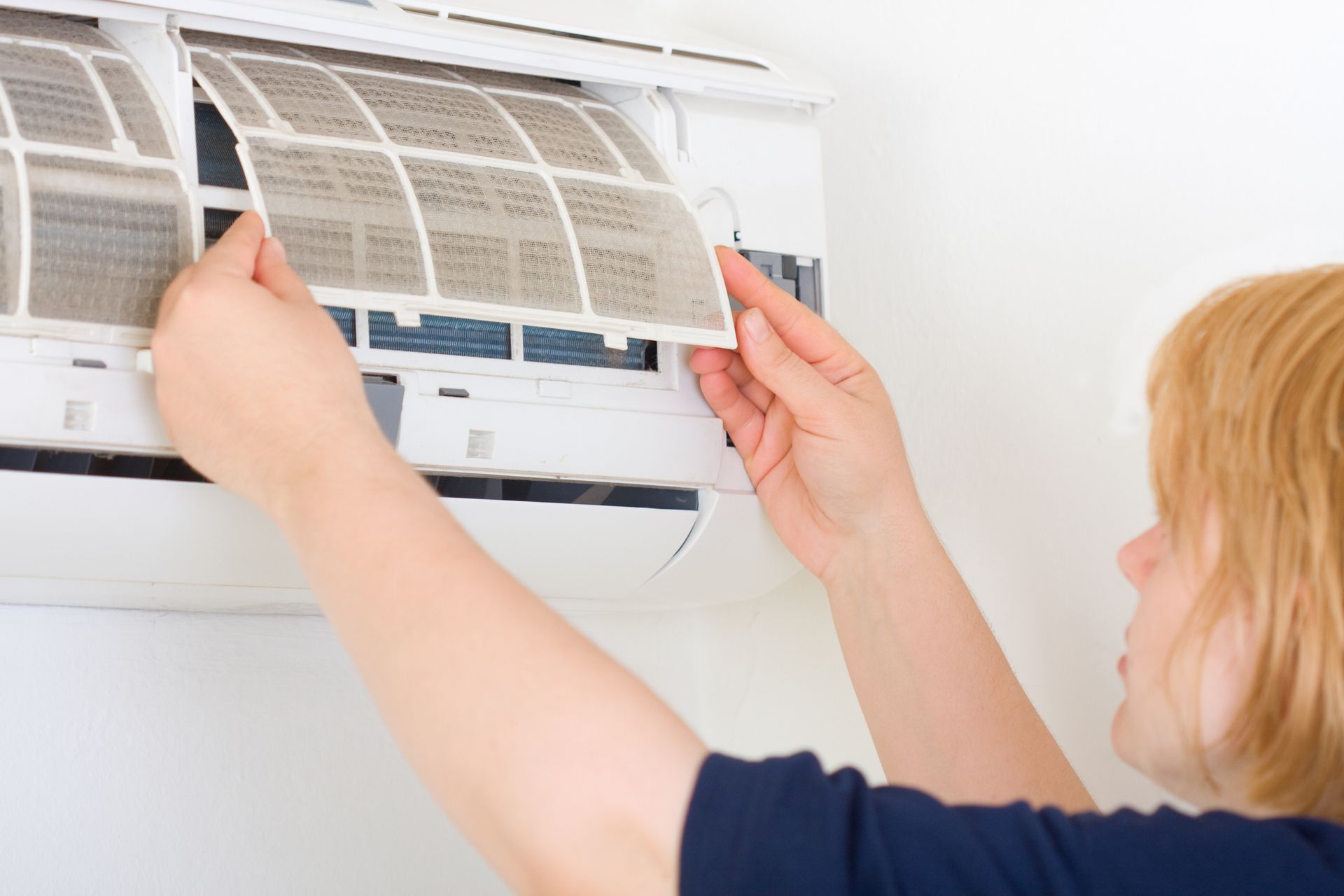 Homeowner removing and replacing dirty AC air filter during summer HVAC maintenance.