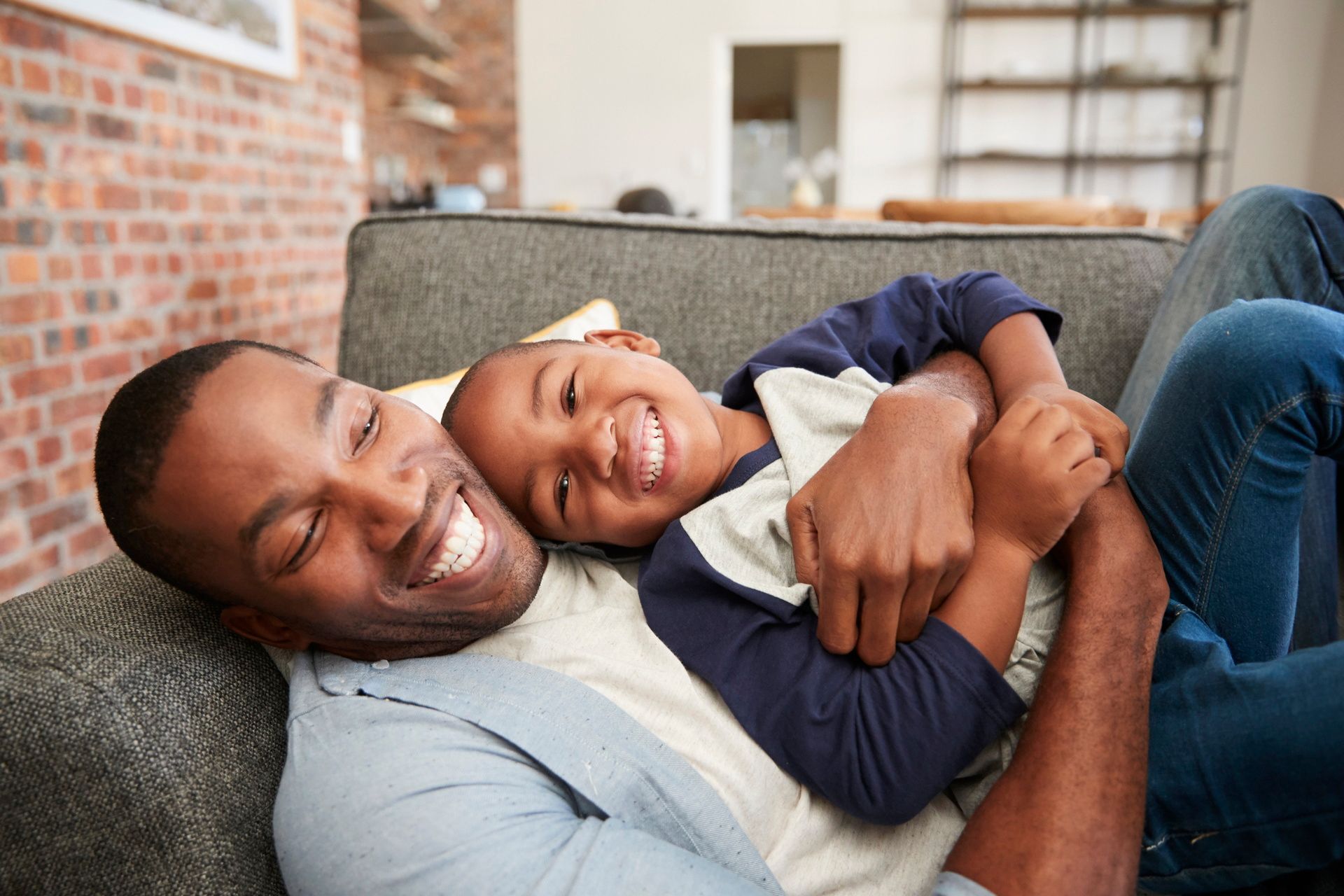Two people cuddling on a gray couch, smiling in a cozy living room
