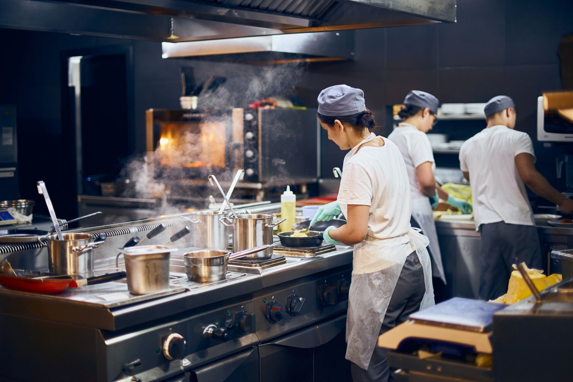 Chefs working in a busy commercial kitchen with pots, steam, and stainless steel counters