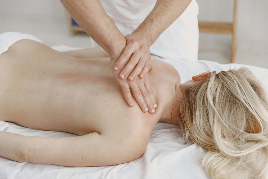 A massage therapist applies pressure to a person's upper back on a massage table.