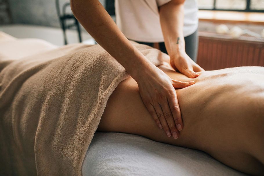 A massage therapist performs deep tissue work on a person's lower back on a treatment table.