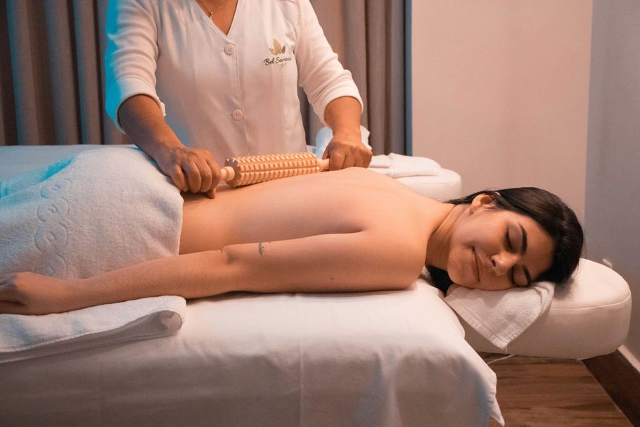 A practitioner uses a wooden roller tool to massage the back of a client resting on a spa treatment table.