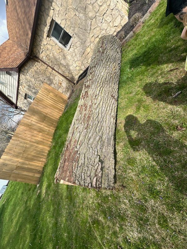 A weathered wooden slab and plywood planks lie on green grass near a stone house.