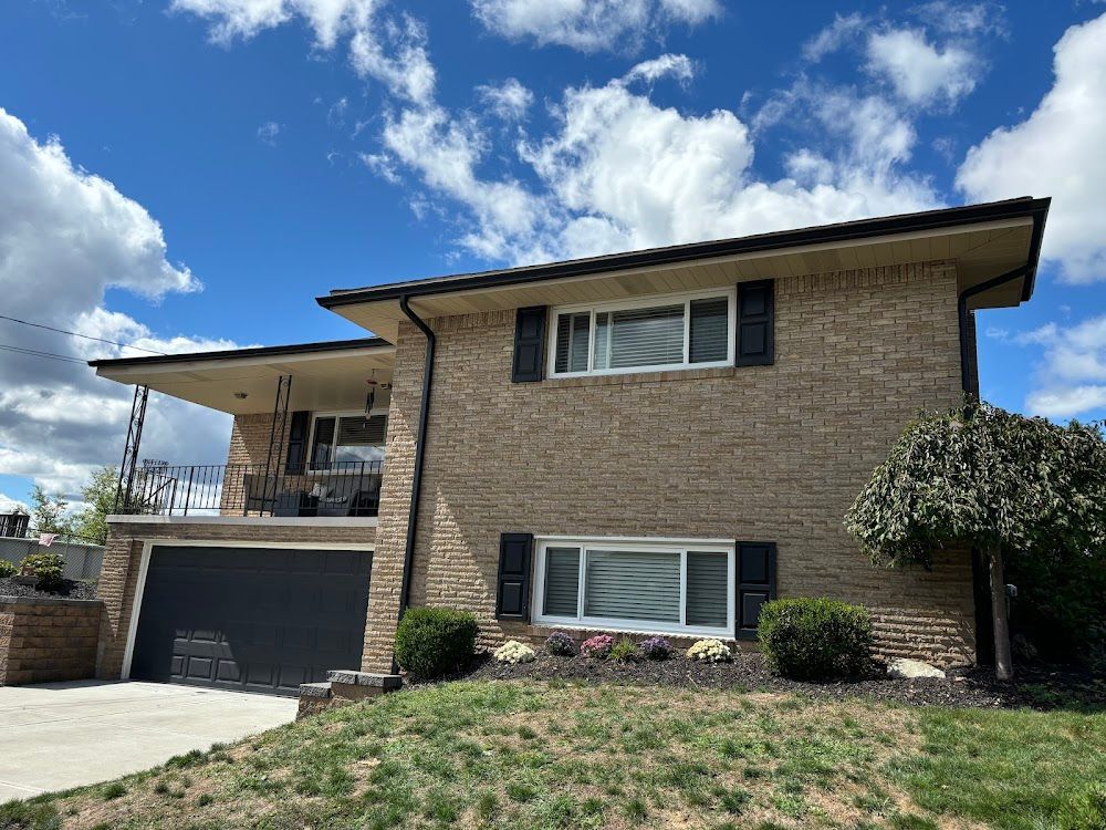 Two-story brick house with a black garage door and shutters under a blue sky with clouds.