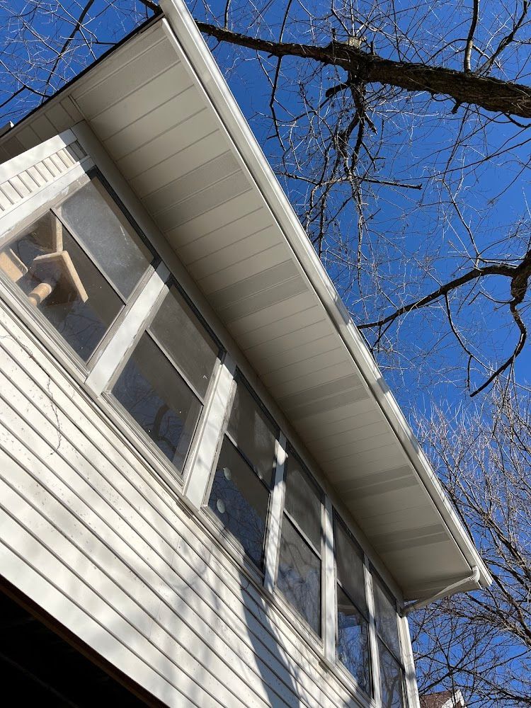 White house exterior with windows, siding, and roof against a blue sky with tree branches.