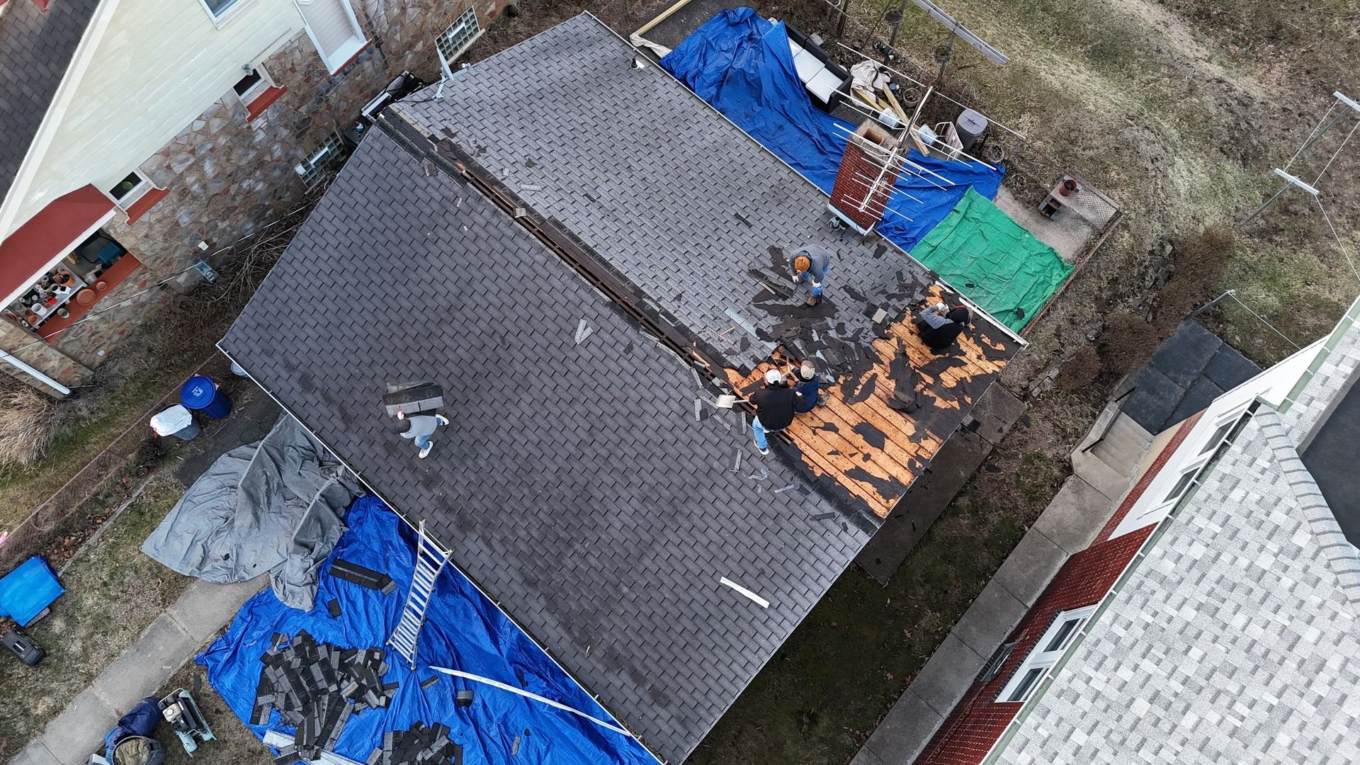 Aerial view of a damaged roof covered by tarps after a storm. Debris scattered around the house.
