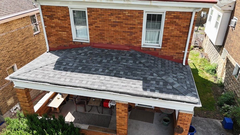 Brick house with porch and asphalt shingle roof. Second story has two windows. Neighboring buildings visible.