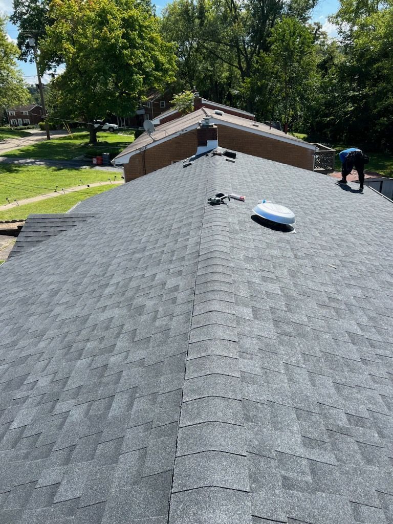 Black asphalt shingle roof, person standing, sunny day, residential neighborhood.