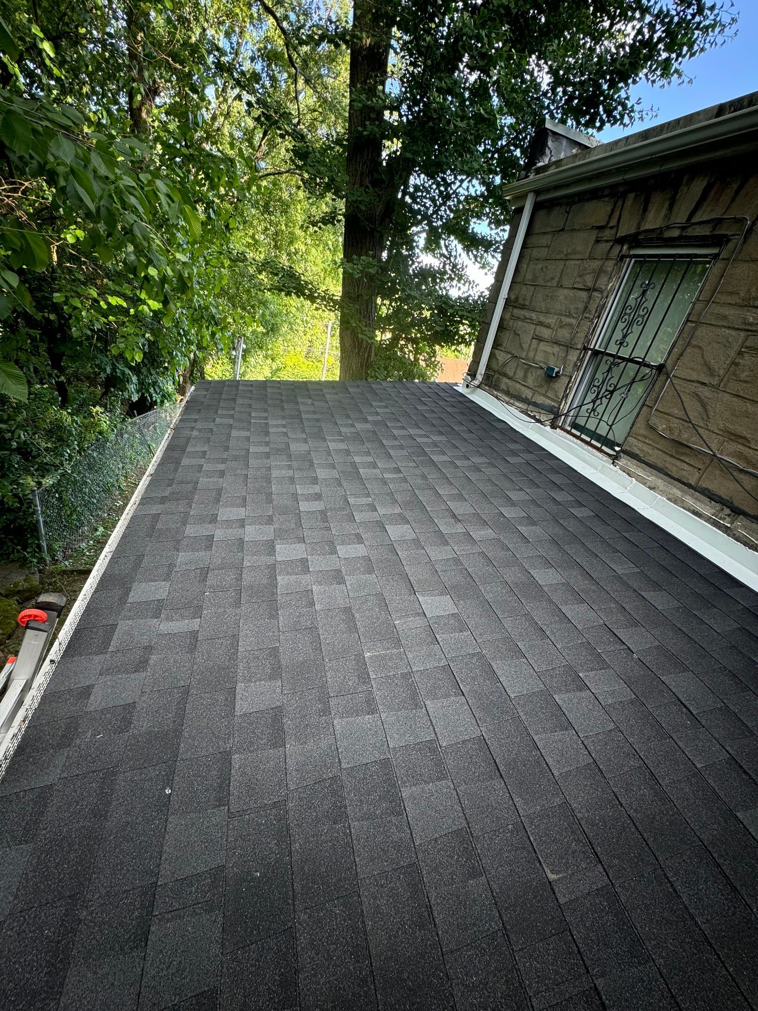 Dark shingled roof with a white gutter, adjacent to a tree and house with a brown wall.