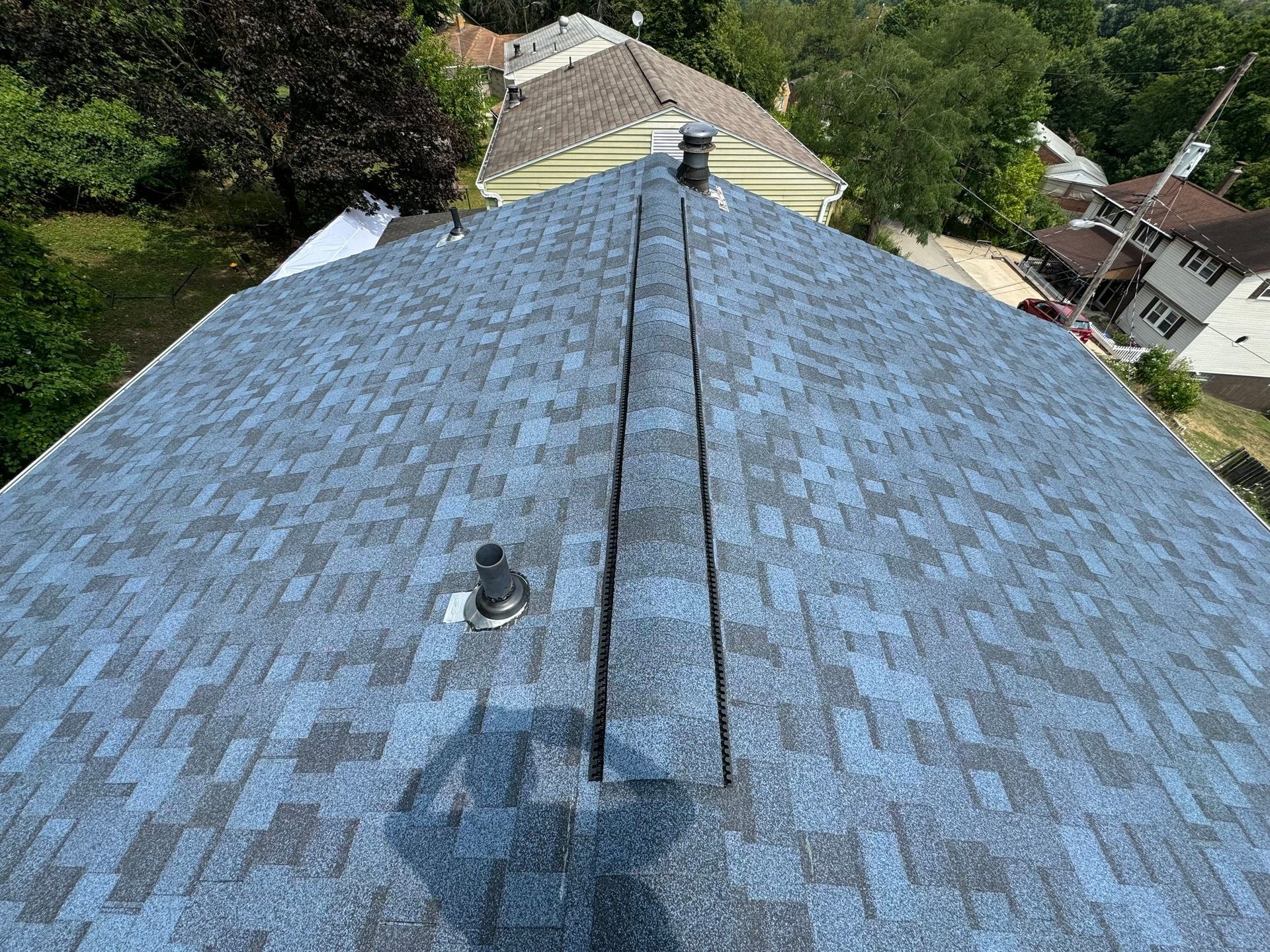 Blue asphalt shingle roof with two vents and a chimney, viewed from above on a sunny day.
