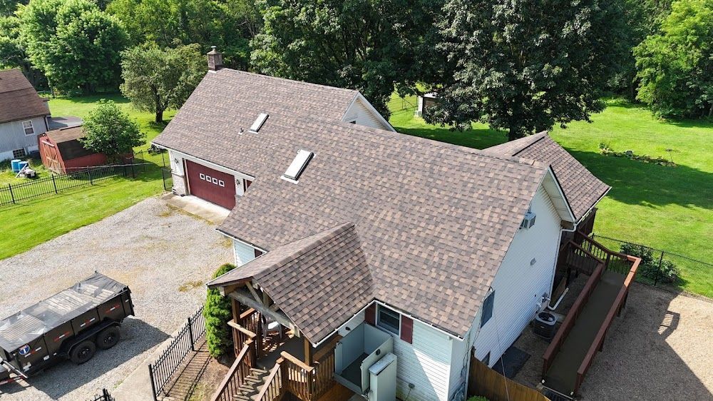 Brown-shingled house with detached garage, wooden deck, and open grassy field in the background.