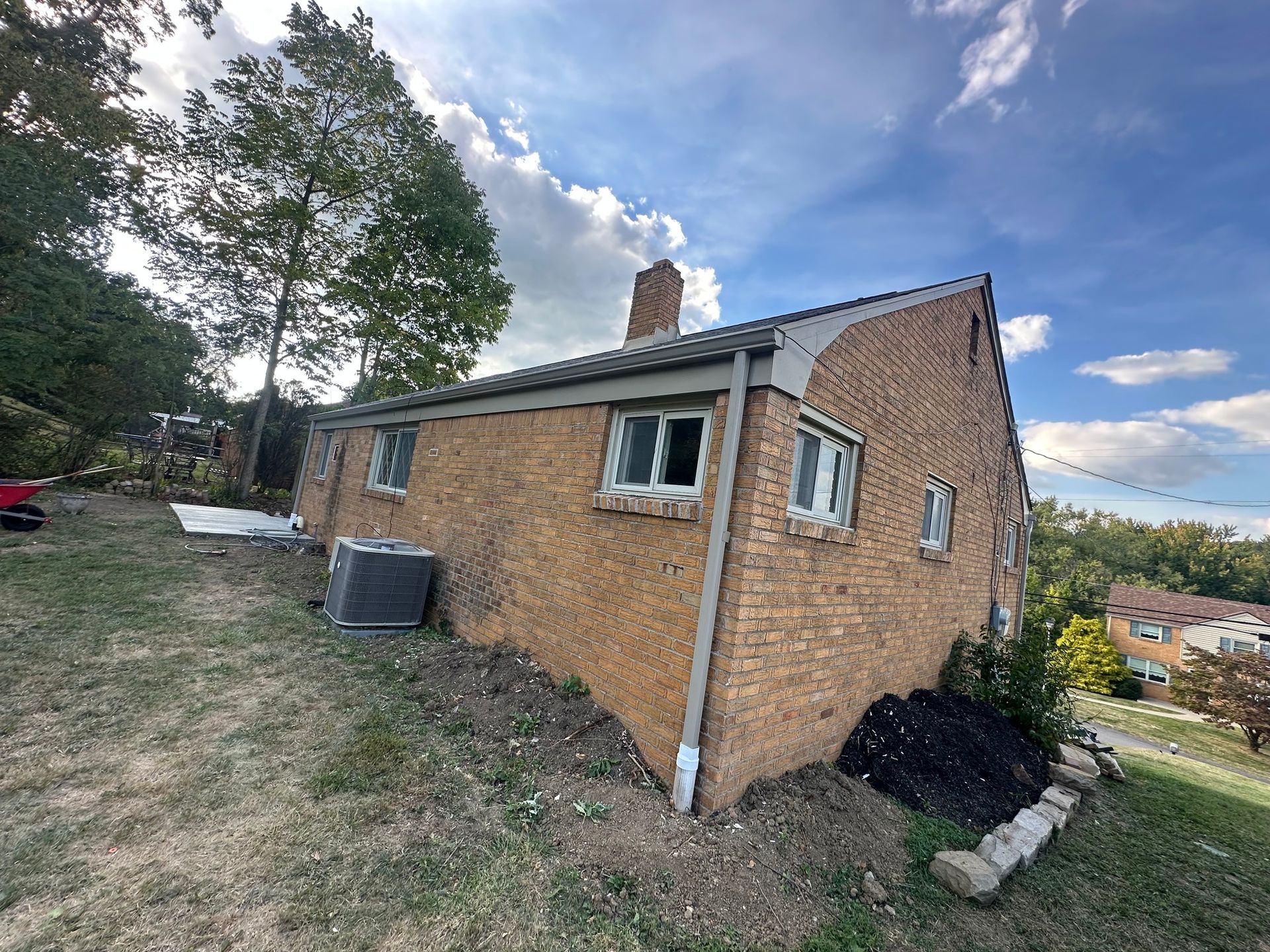Brick house on a hillside with a chimney, windows, and an air conditioner unit. Overcast sky.