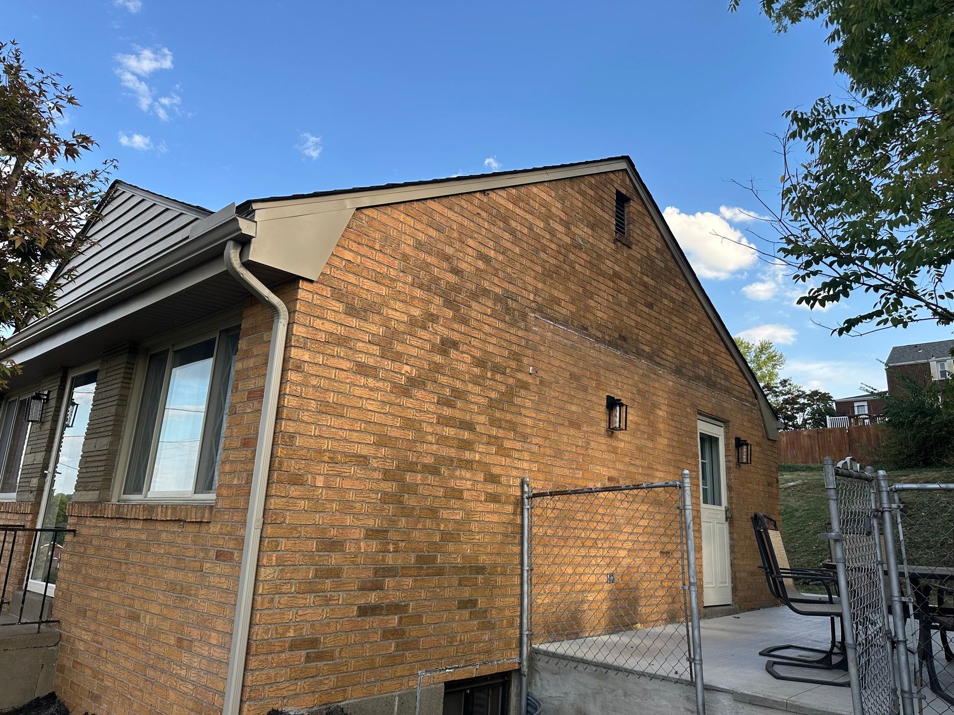 Brick house exterior with a small door, window, and small deck. Blue sky.