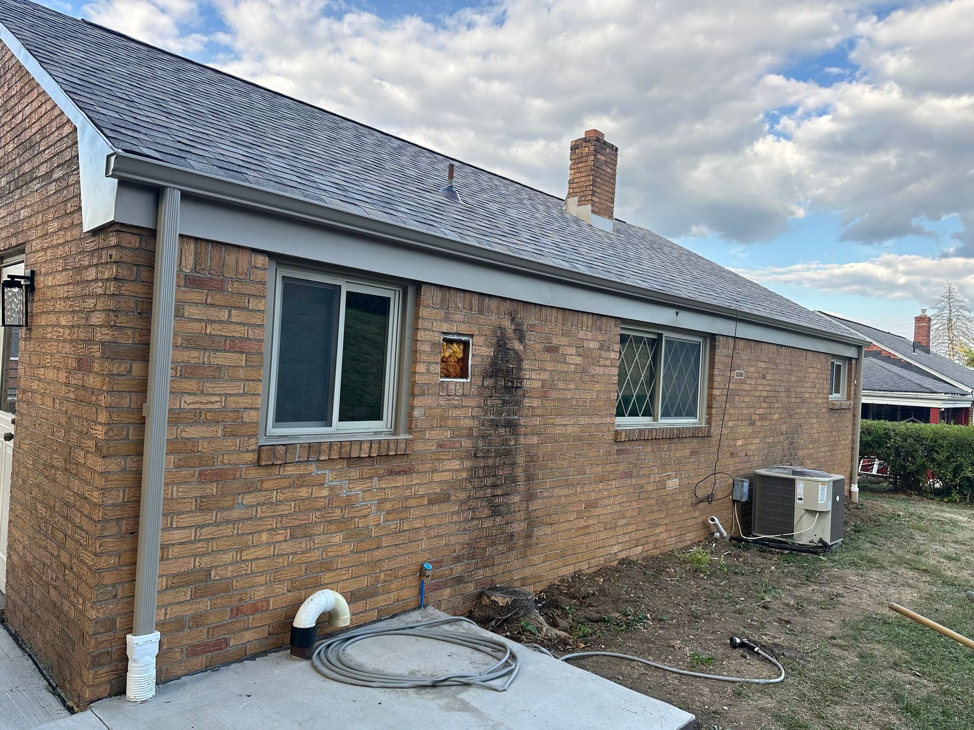 Brick building exterior with gray roof, windows, and air conditioning unit.