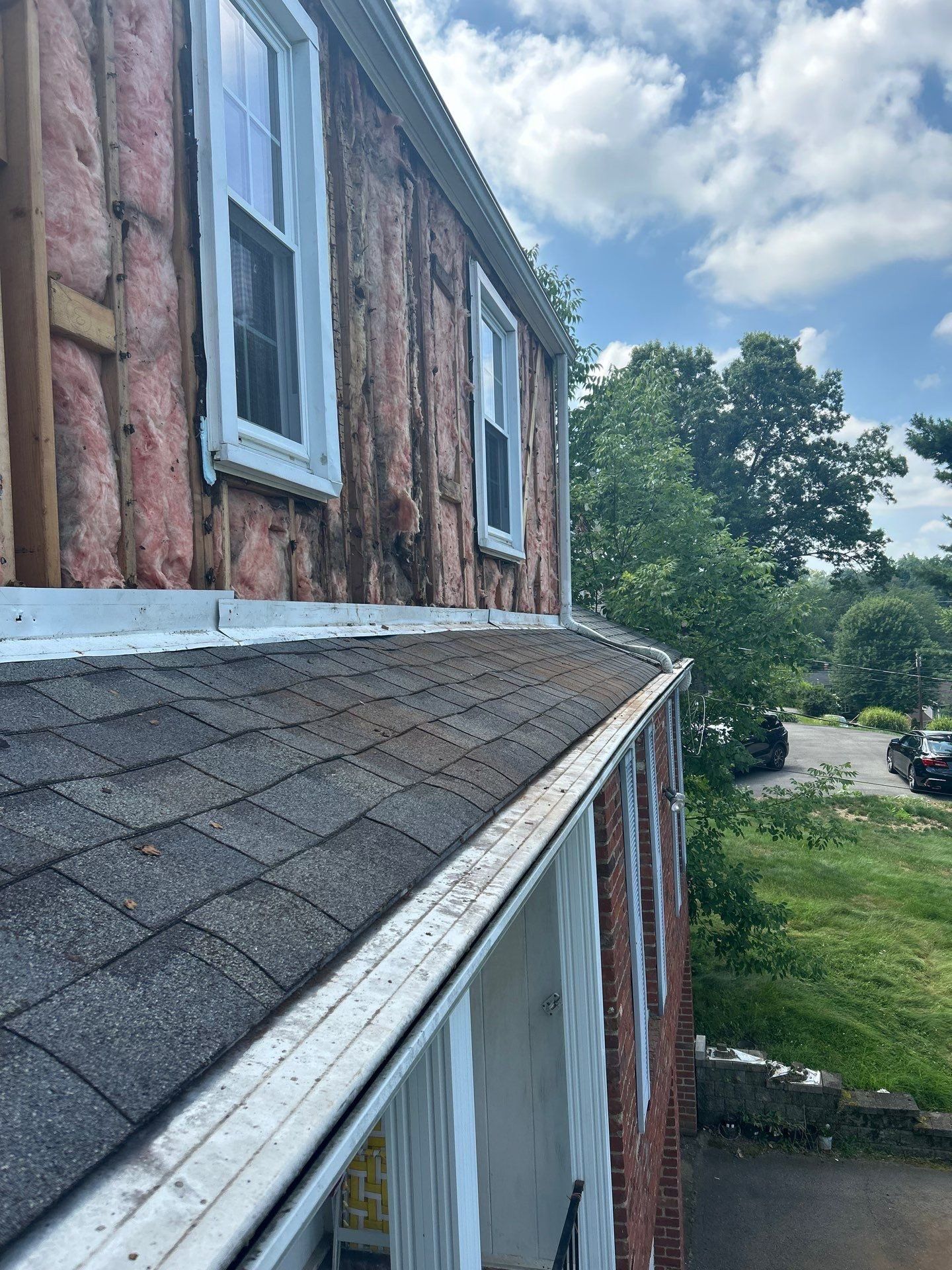Exterior of a building under construction, showing a roof, windows, and exposed insulation. Cloudy sky.