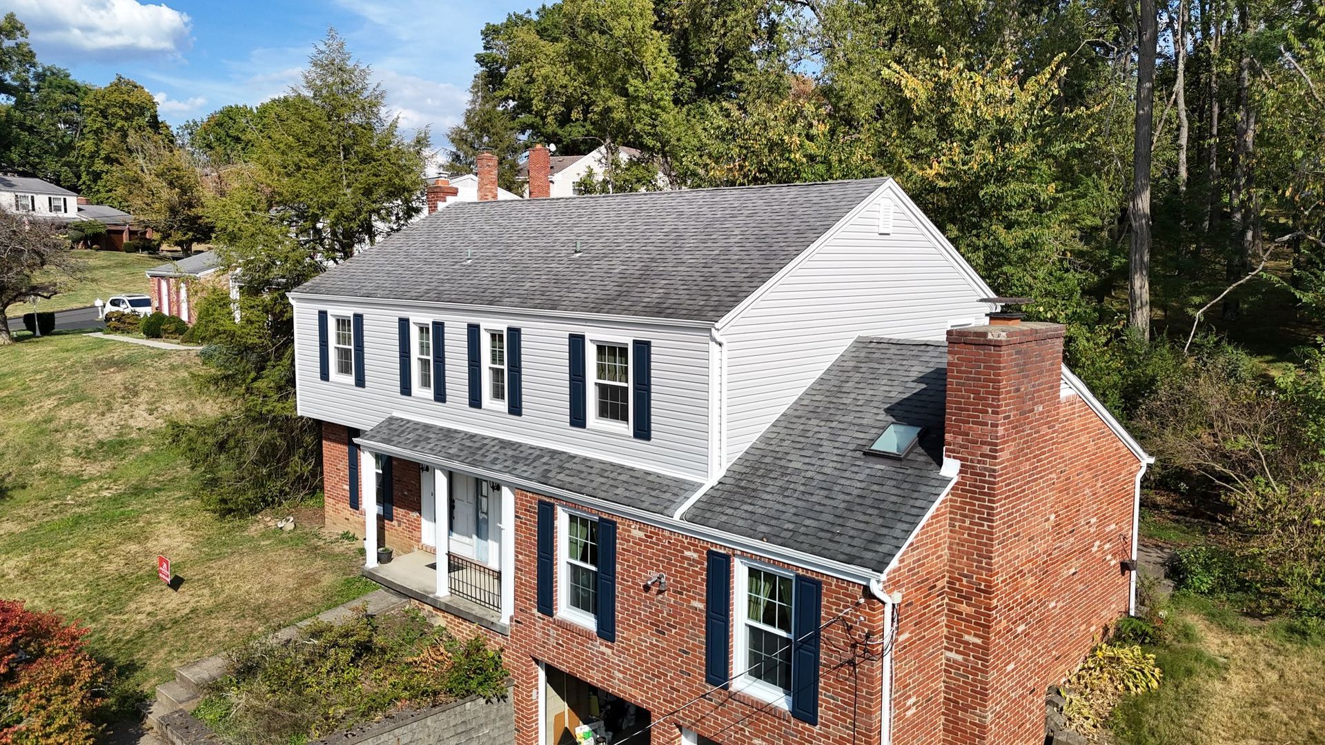 Two-story brick house with gray roof and blue shutters, surrounded by trees.