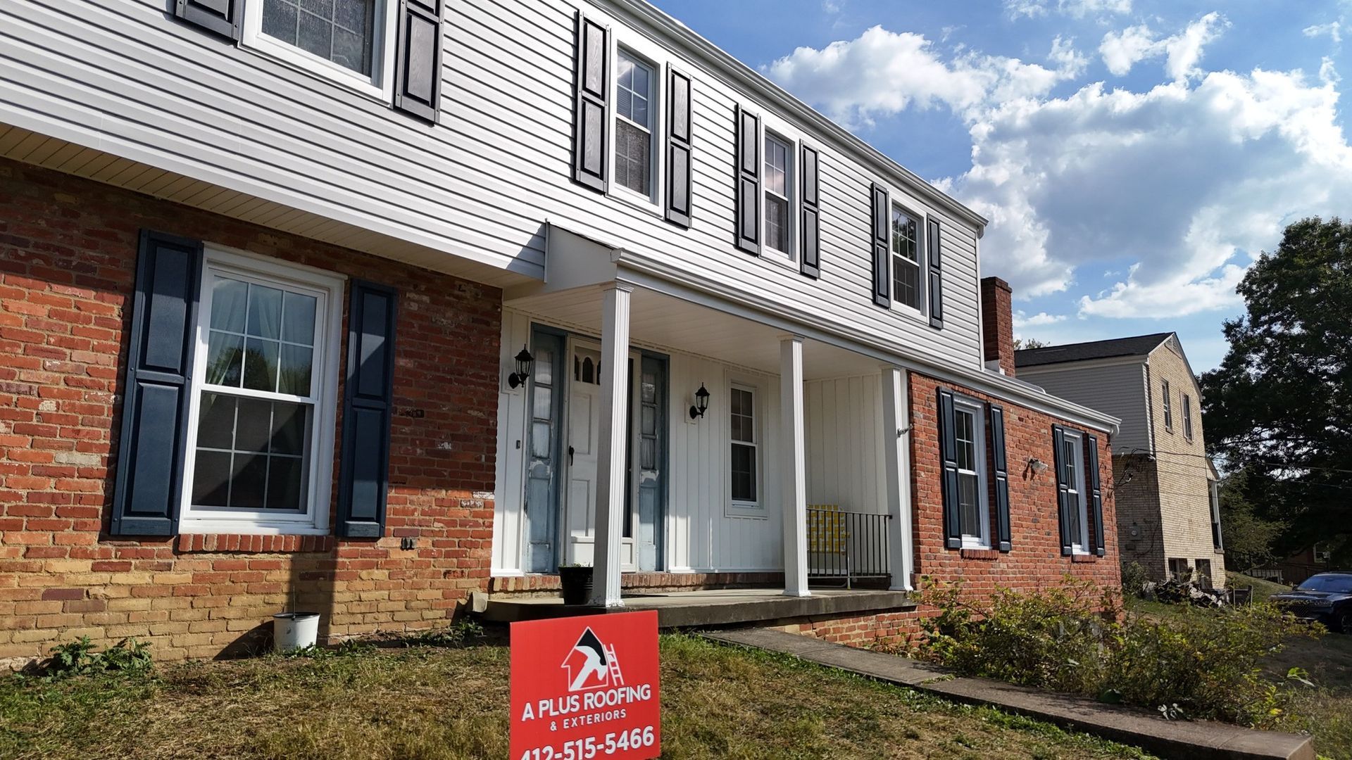 Two-story house with white siding and brick facade. Blue shutters and a porch with white columns.