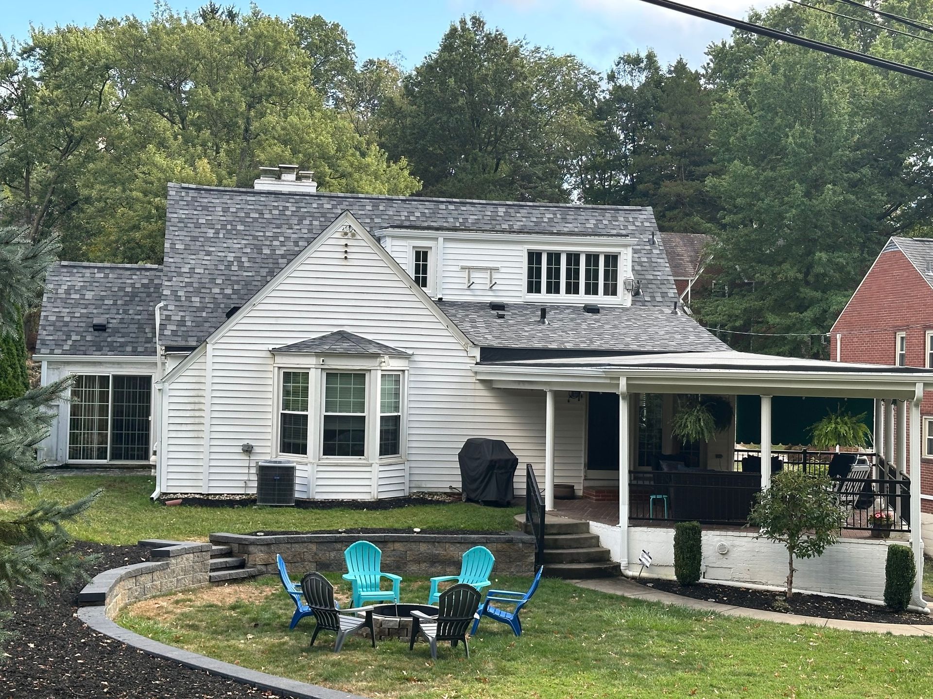 White house with porch and seating in front yard, trees in background.