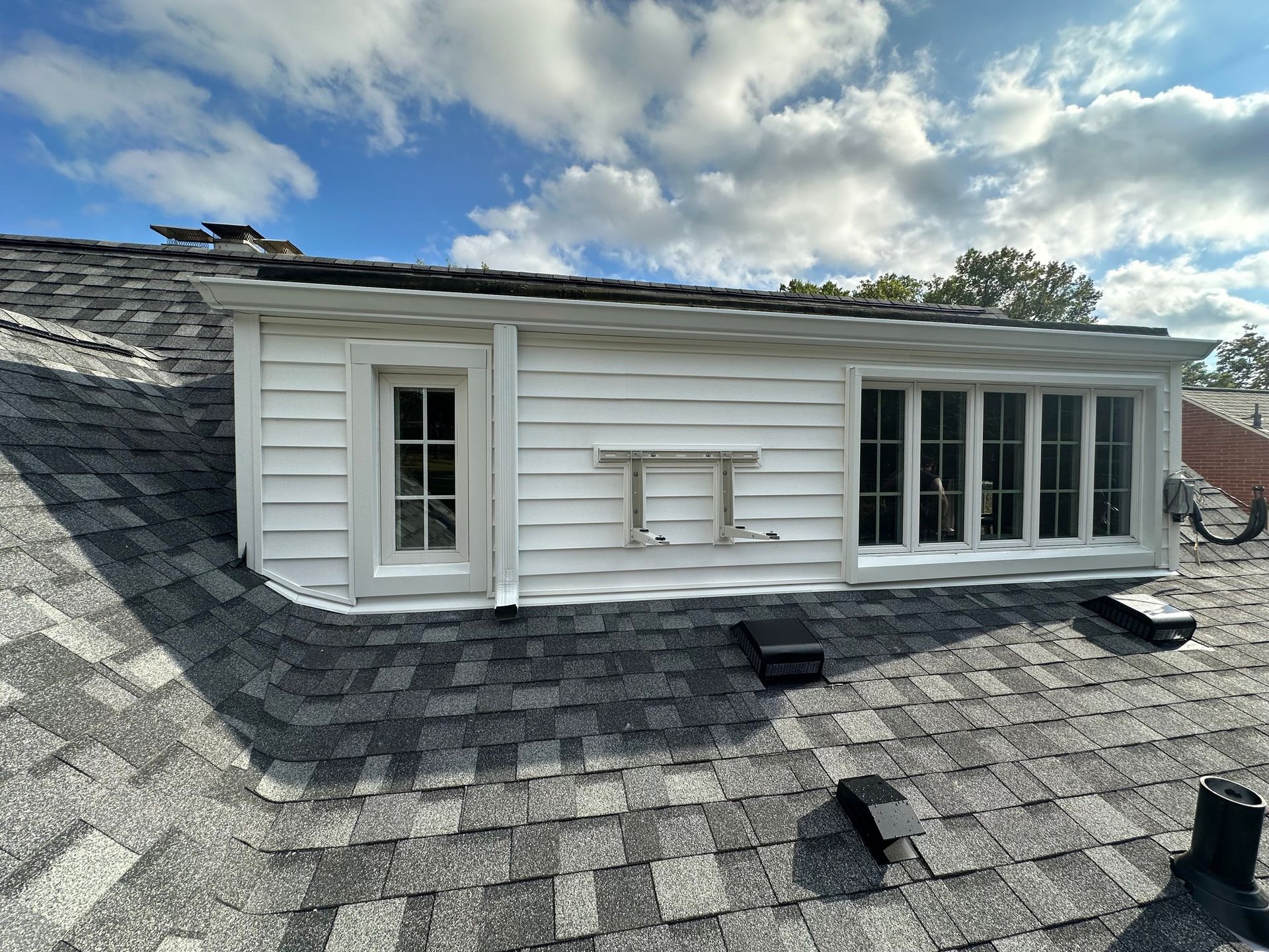 White dormer with windows on a shingled roof under a cloudy sky.
