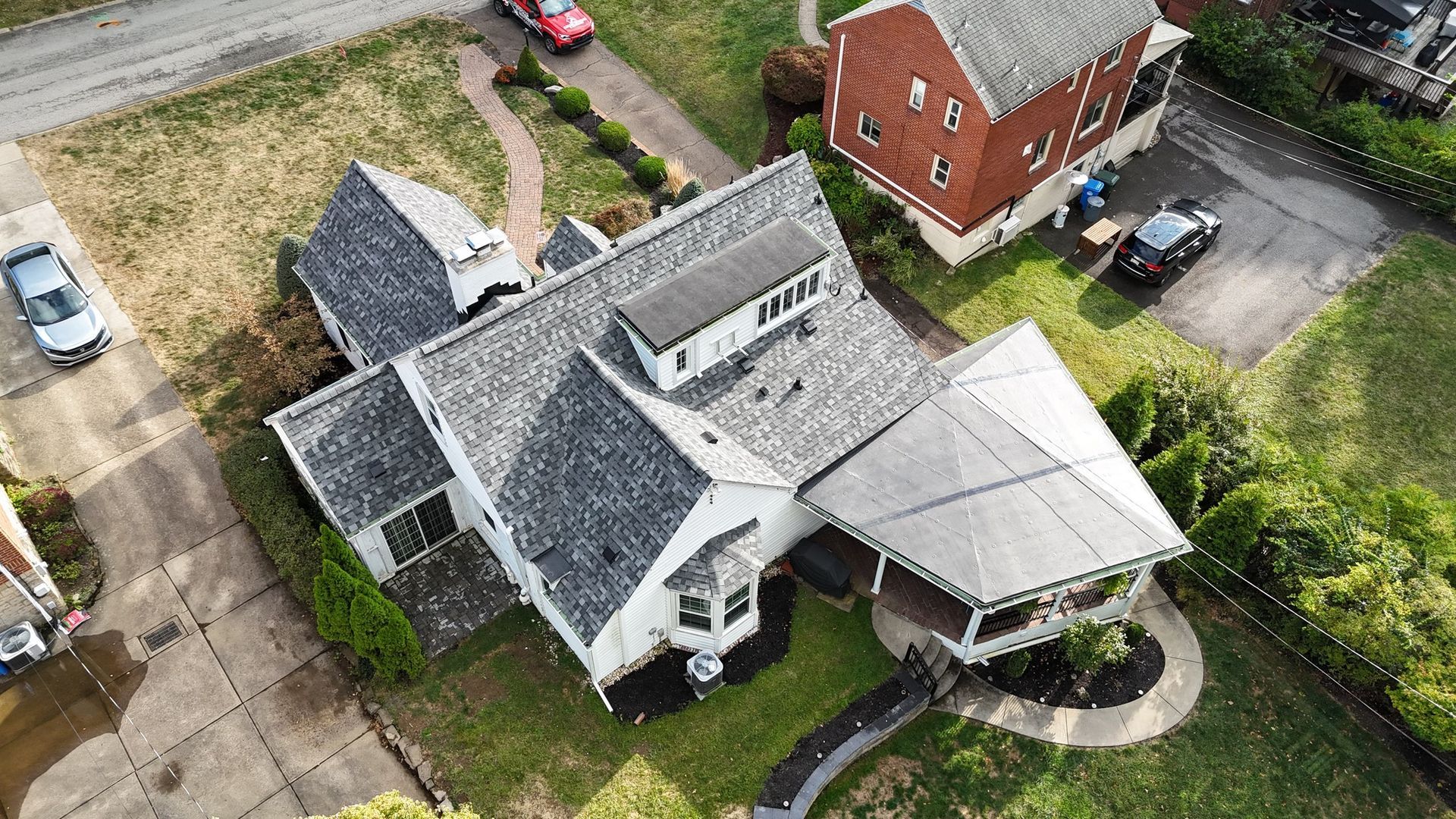 Overhead view of a white house with a gray roof and a porch, surrounded by a lawn and adjacent to a driveway.