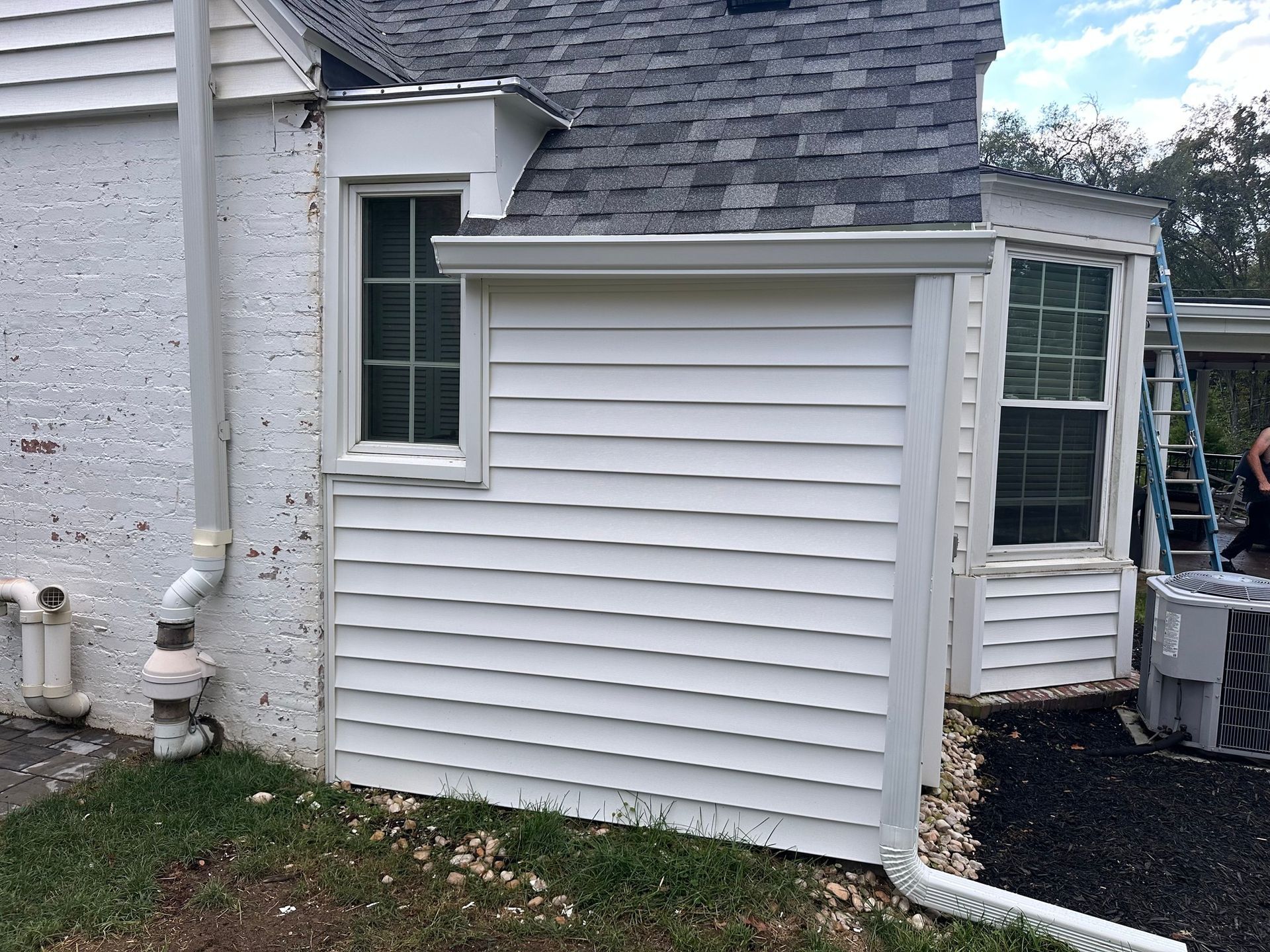 White house exterior with new siding, gutters, windows, and a ladder leaning against the roof.