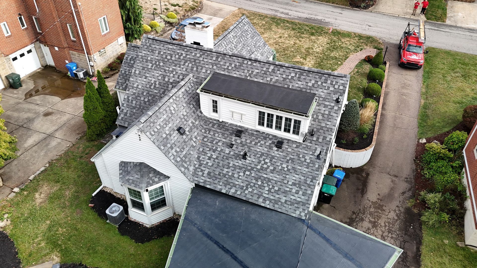 Aerial view of a house with a new gray shingle roof, a flat black roof, and a red truck nearby.