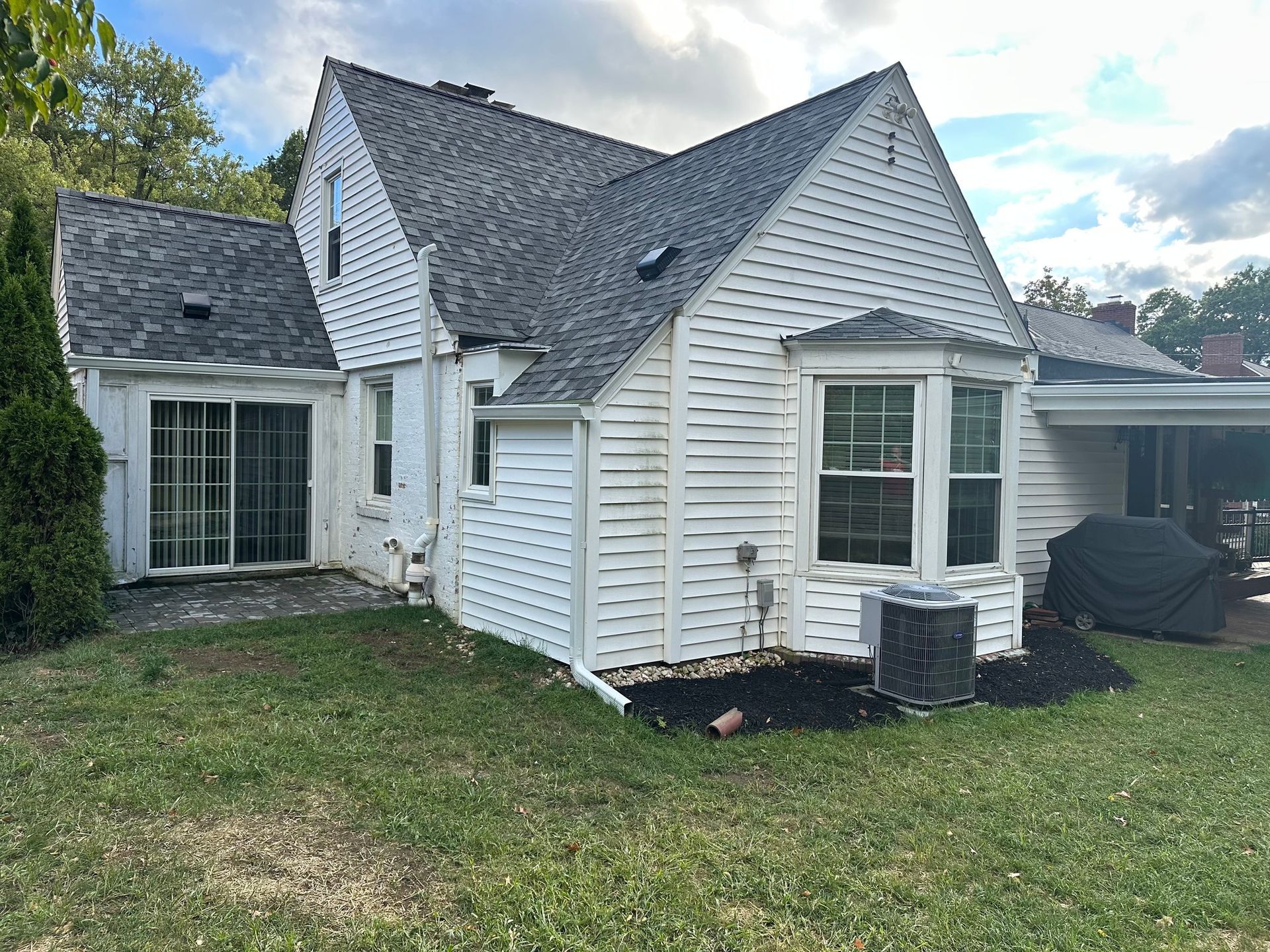 White house with gray roof, sliding glass door, bay window, and a covered patio, set on a green lawn.