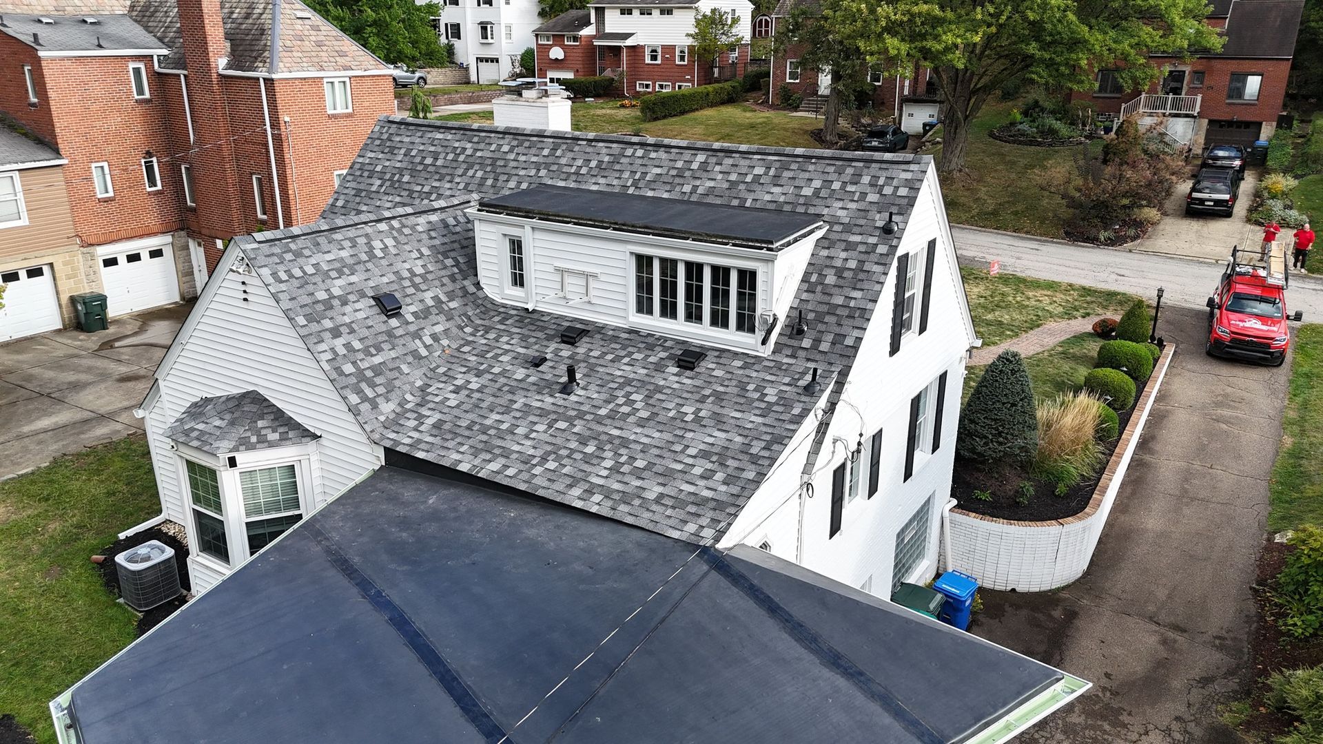 Overhead view of a white two-story house with a gray roof and black shutters. A red truck is parked nearby.
