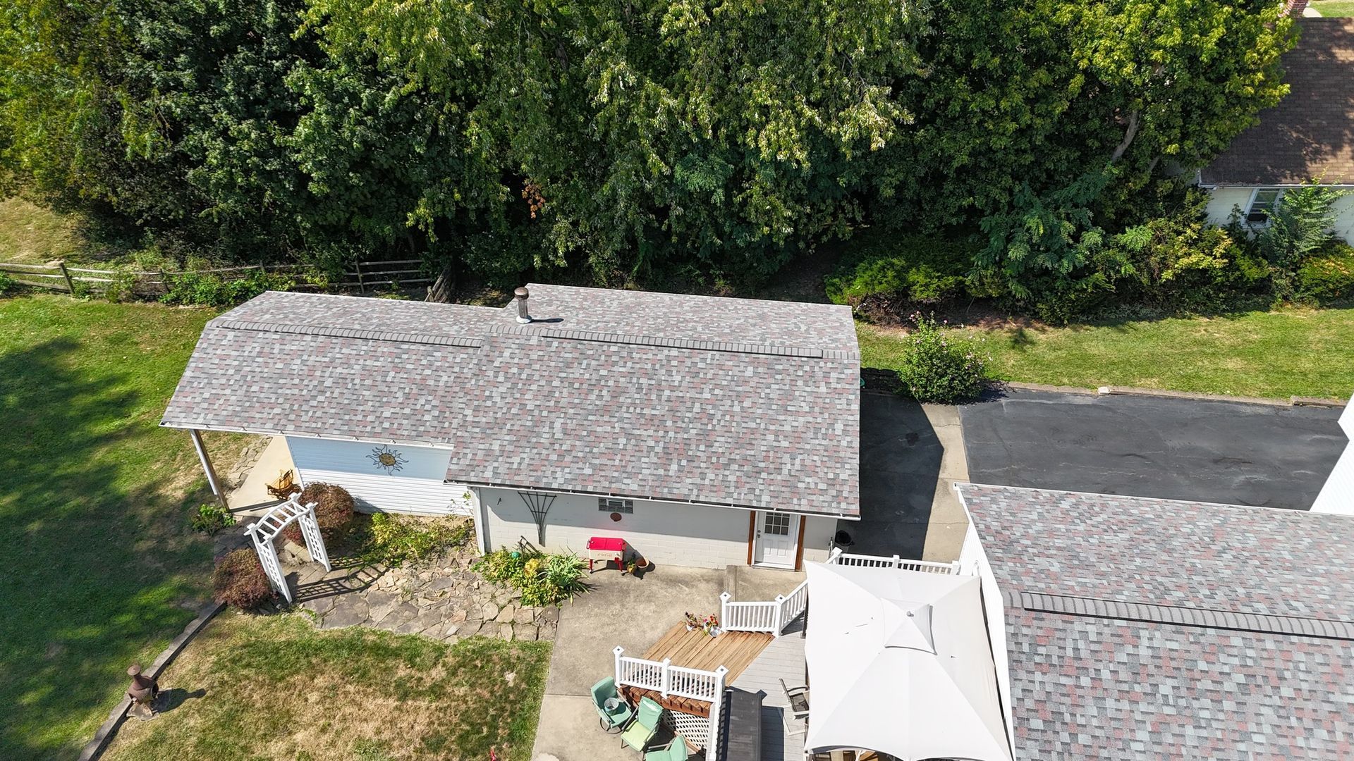 Overhead view of a light-colored house with a textured, gray roof. A deck and driveway are visible.
