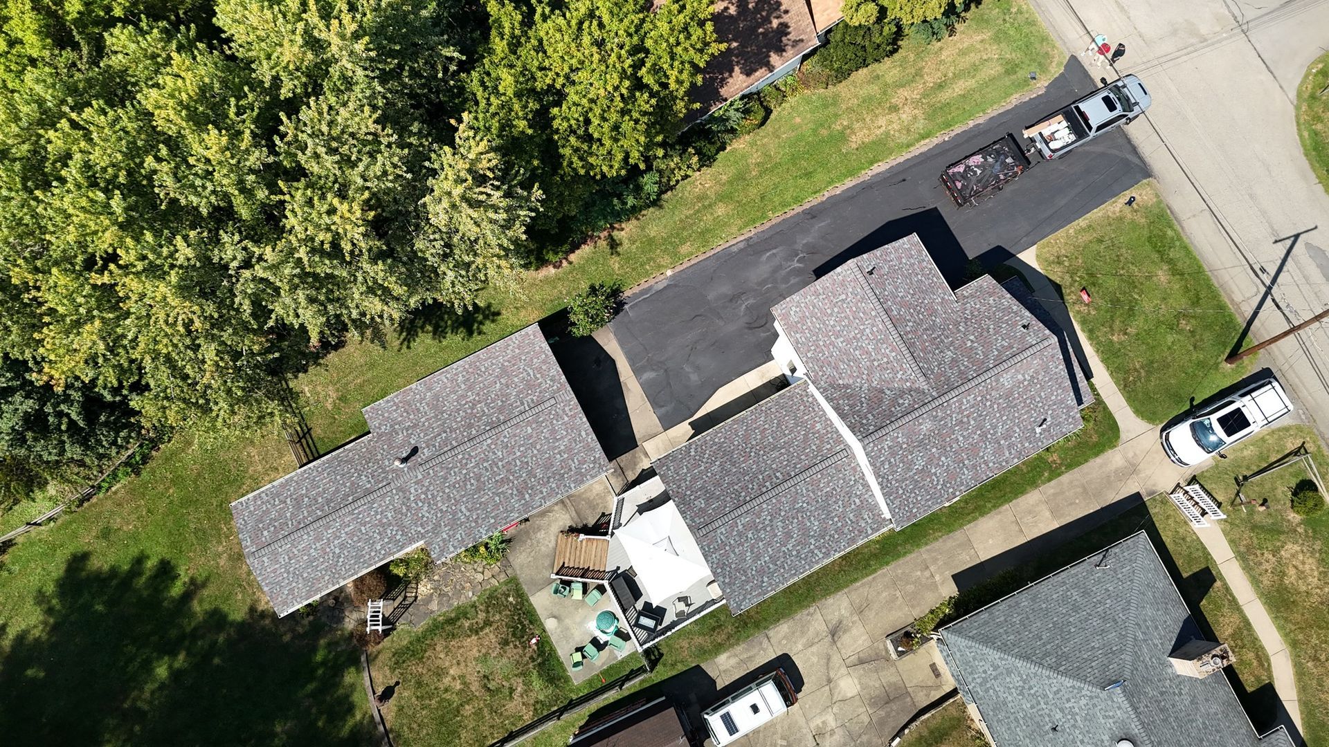 Aerial view of a house with a driveway and car, trees, and grass.