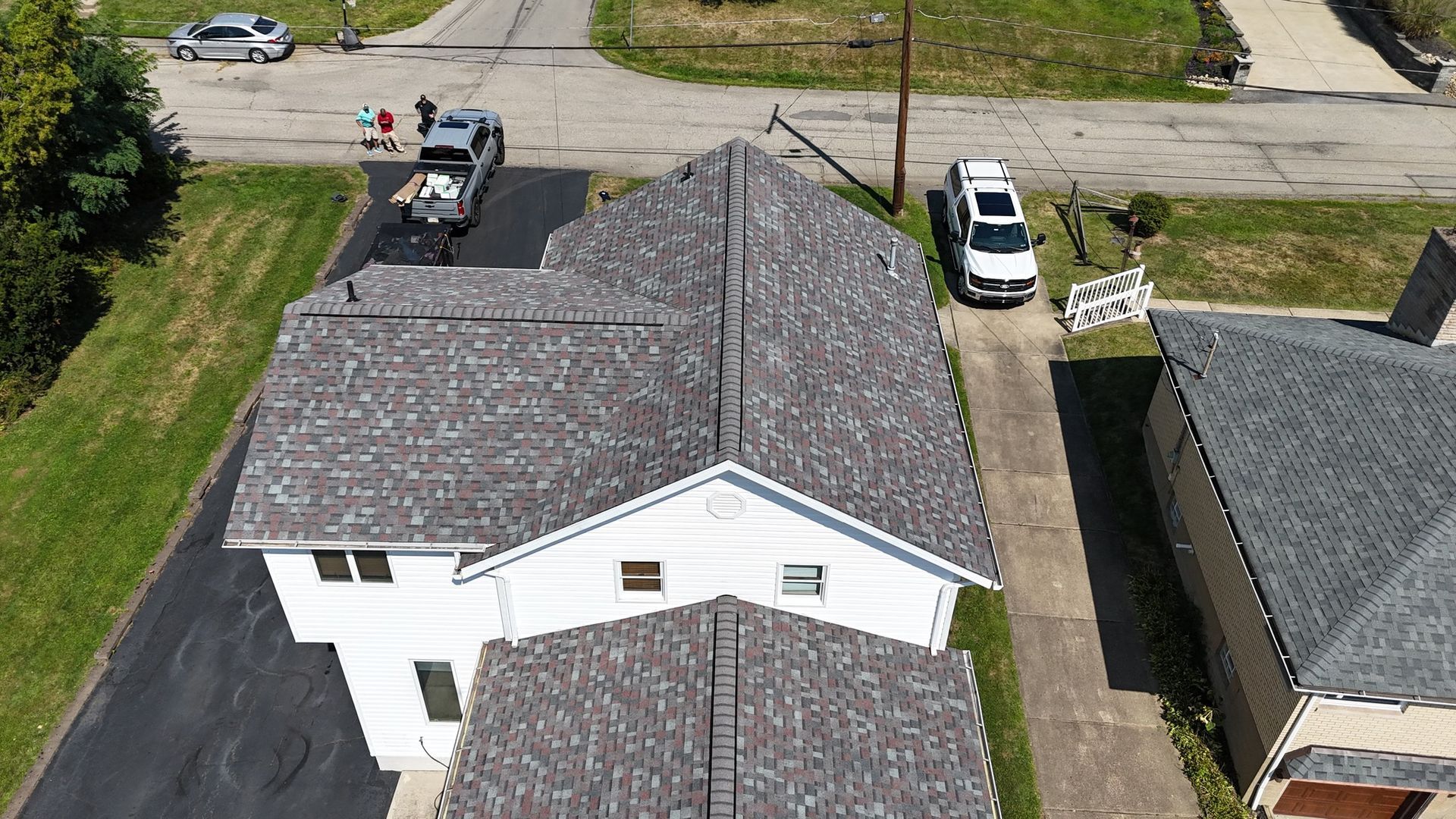 Overhead view of a house with a gray roof, driveway, and cars parked in front.