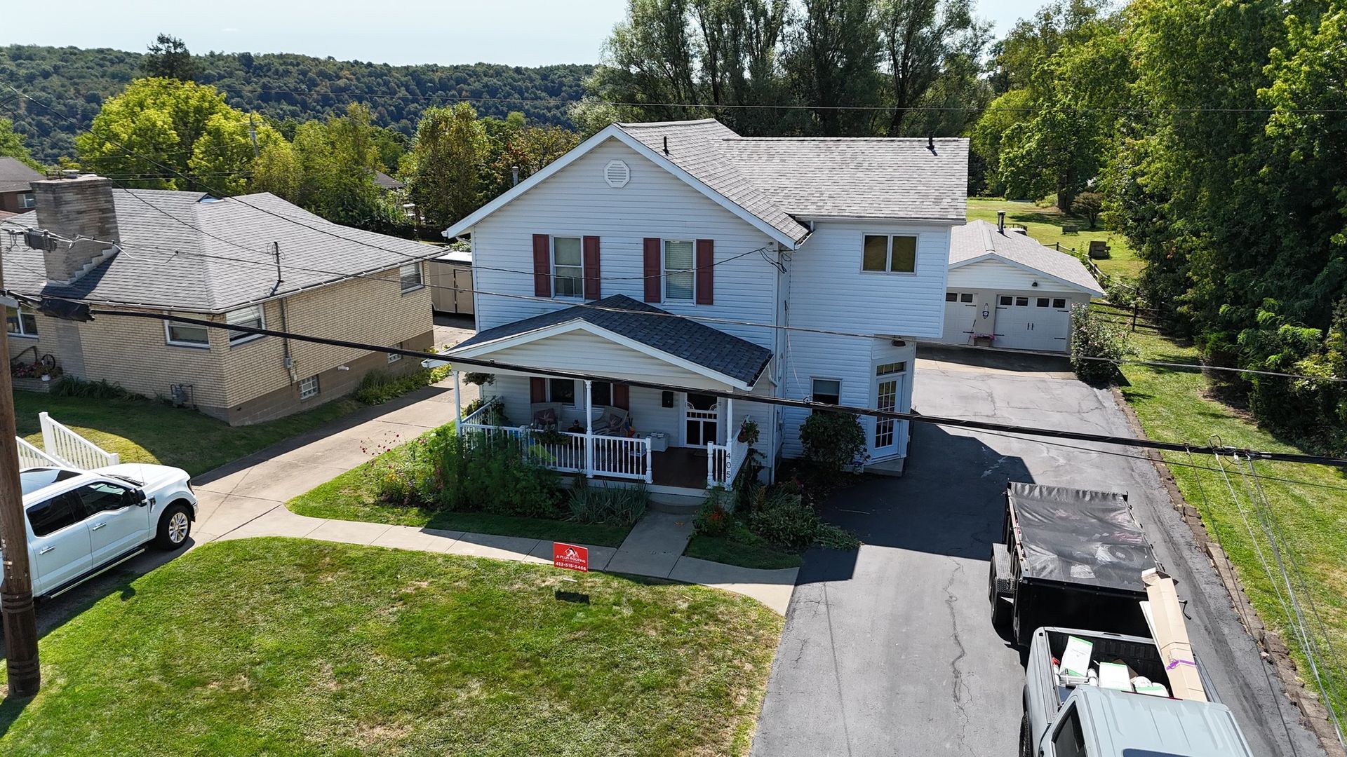 Two-story house with red shutters and a small porch; a white truck and trailer are in the driveway.