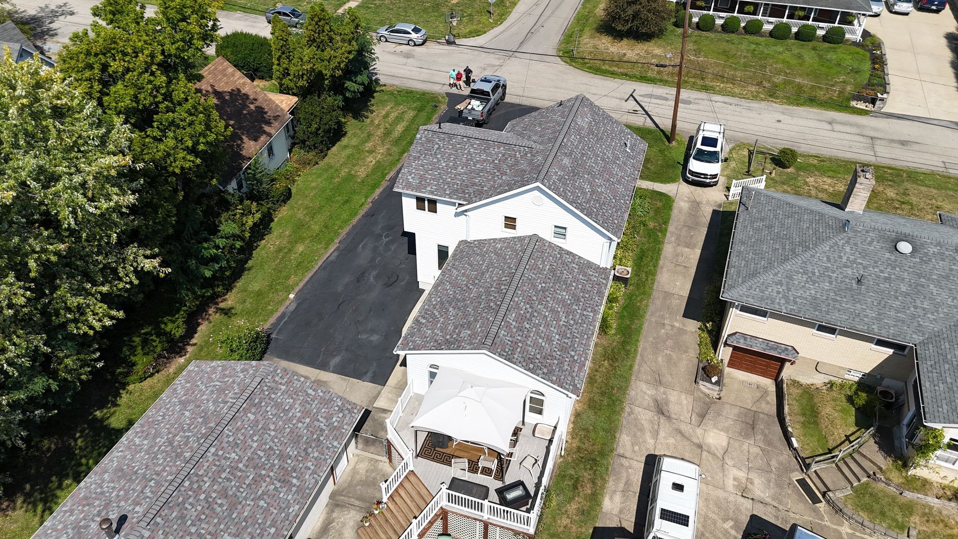 Aerial view of white houses with gray roofs and black driveways. Cars are parked nearby.