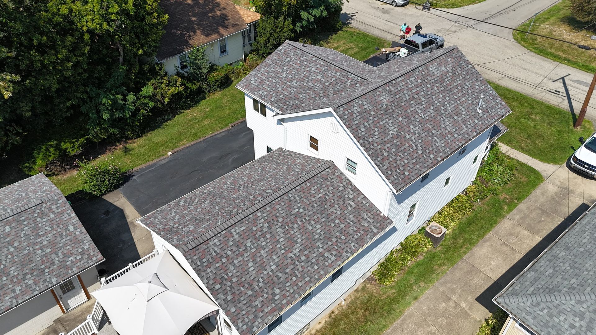 Aerial view of a white house with a gray shingle roof, driveway, and small lawn.