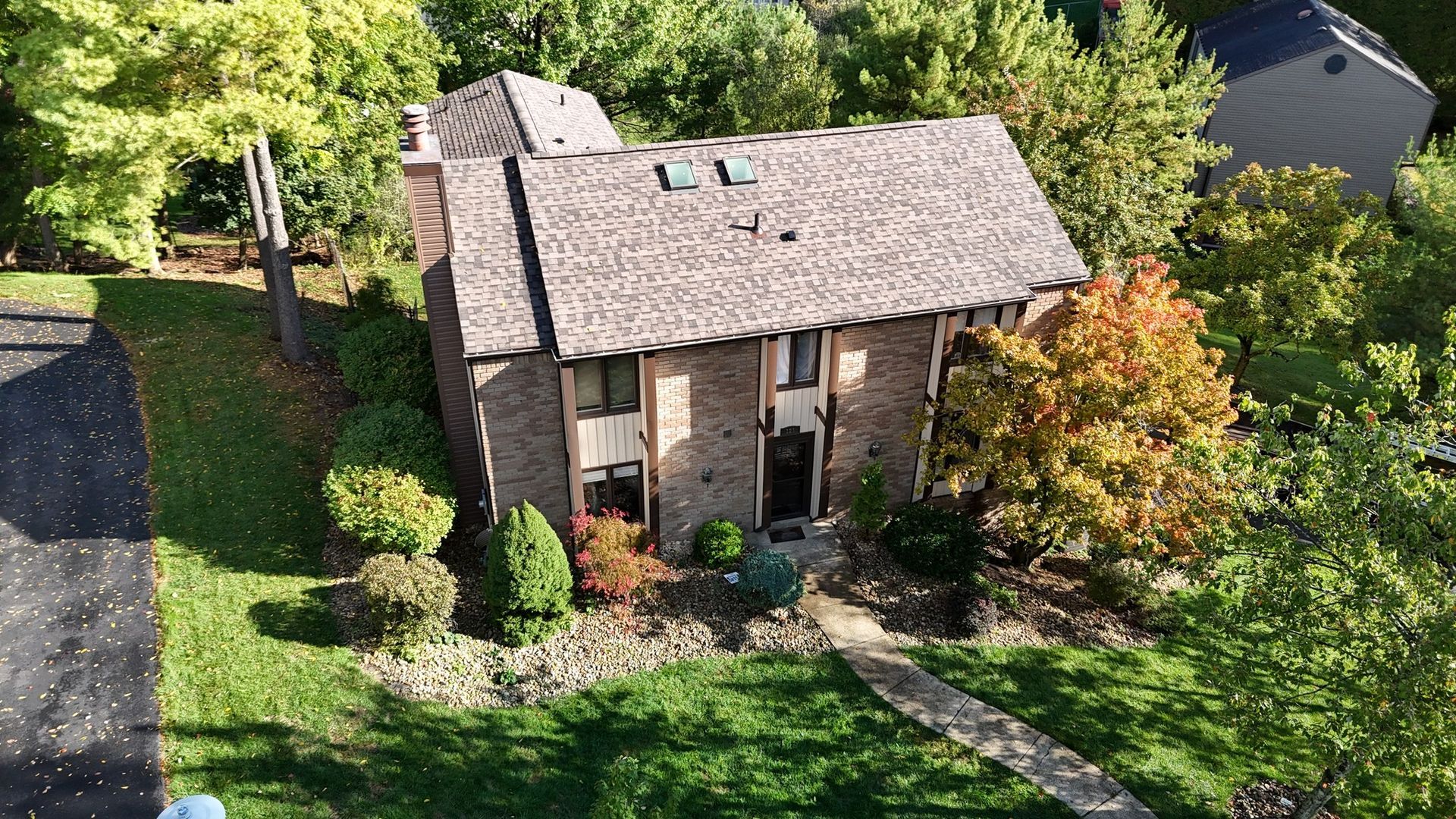 Two-story brick house with brown roof surrounded by green and orange trees.