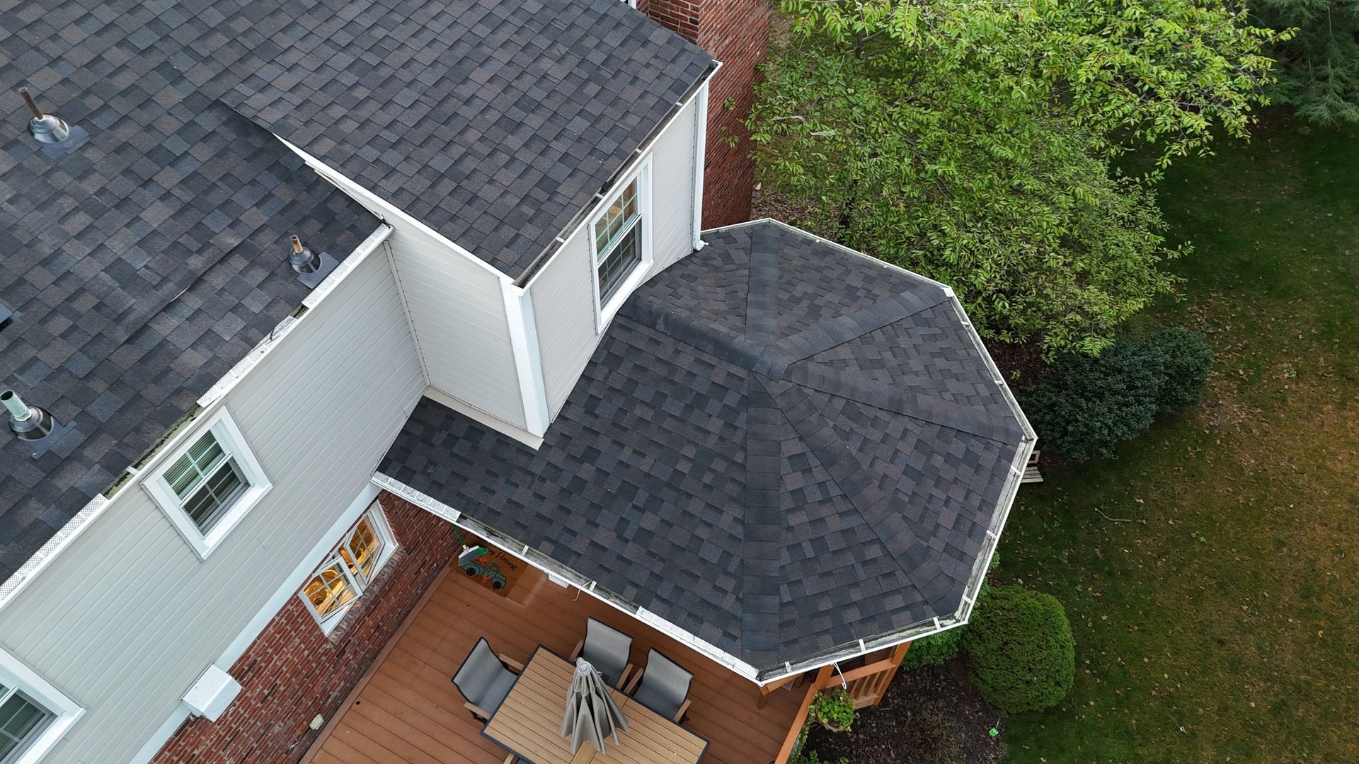 Overhead view of a house with a gray roof and a wooden deck. A table and chairs sit on the deck.