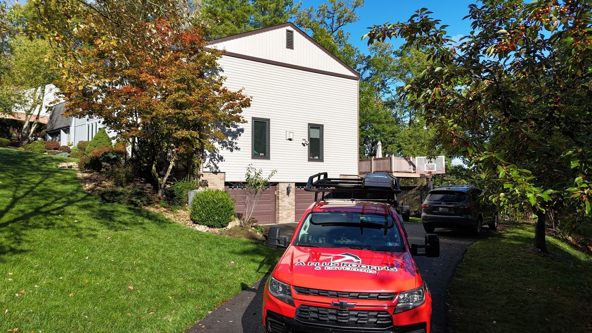 Red SUV parked on a driveway in front of a white house with a car on top. Green grass and trees surround.