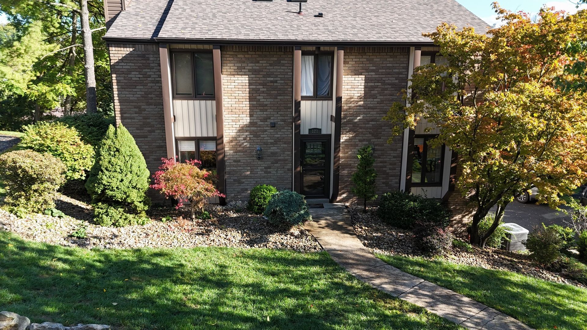 Two-story brick house with a stone pathway leading to the front door, flanked by greenery and trees.