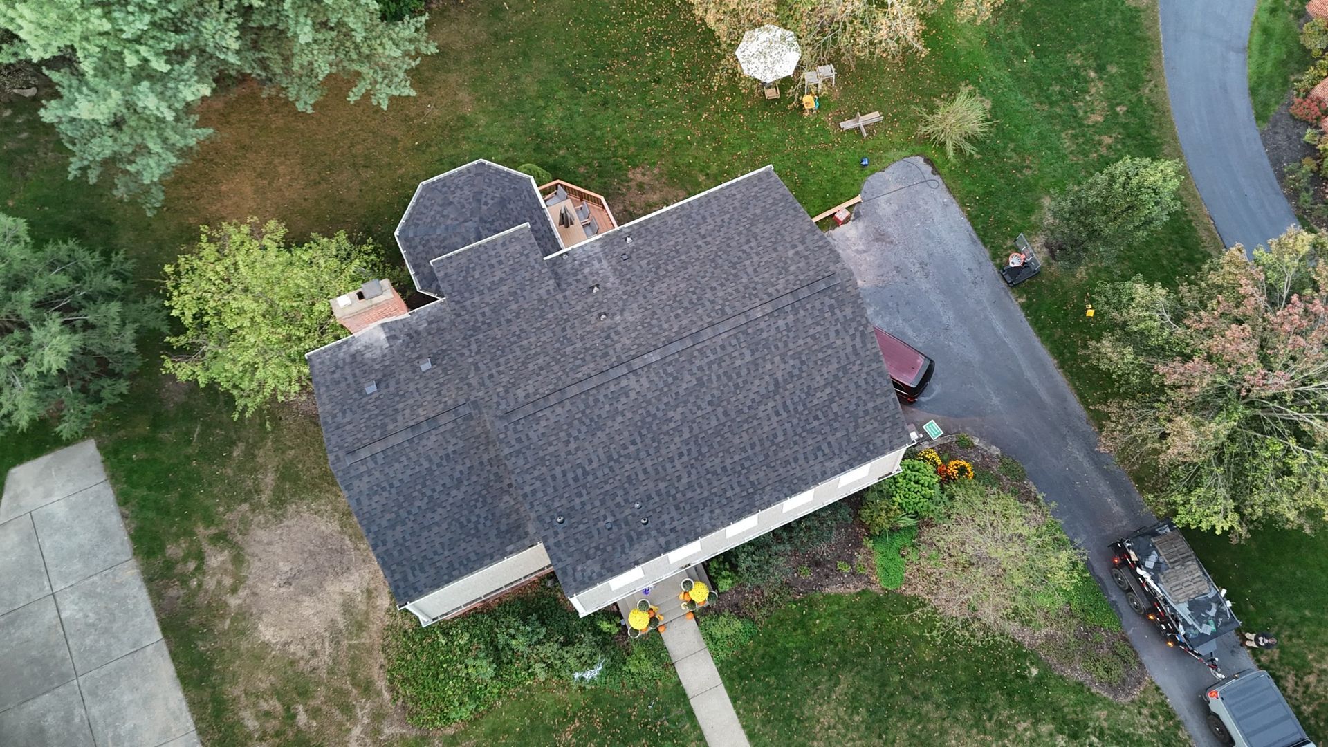 Overhead view of a house with a dark roof and driveway surrounded by grass and trees.